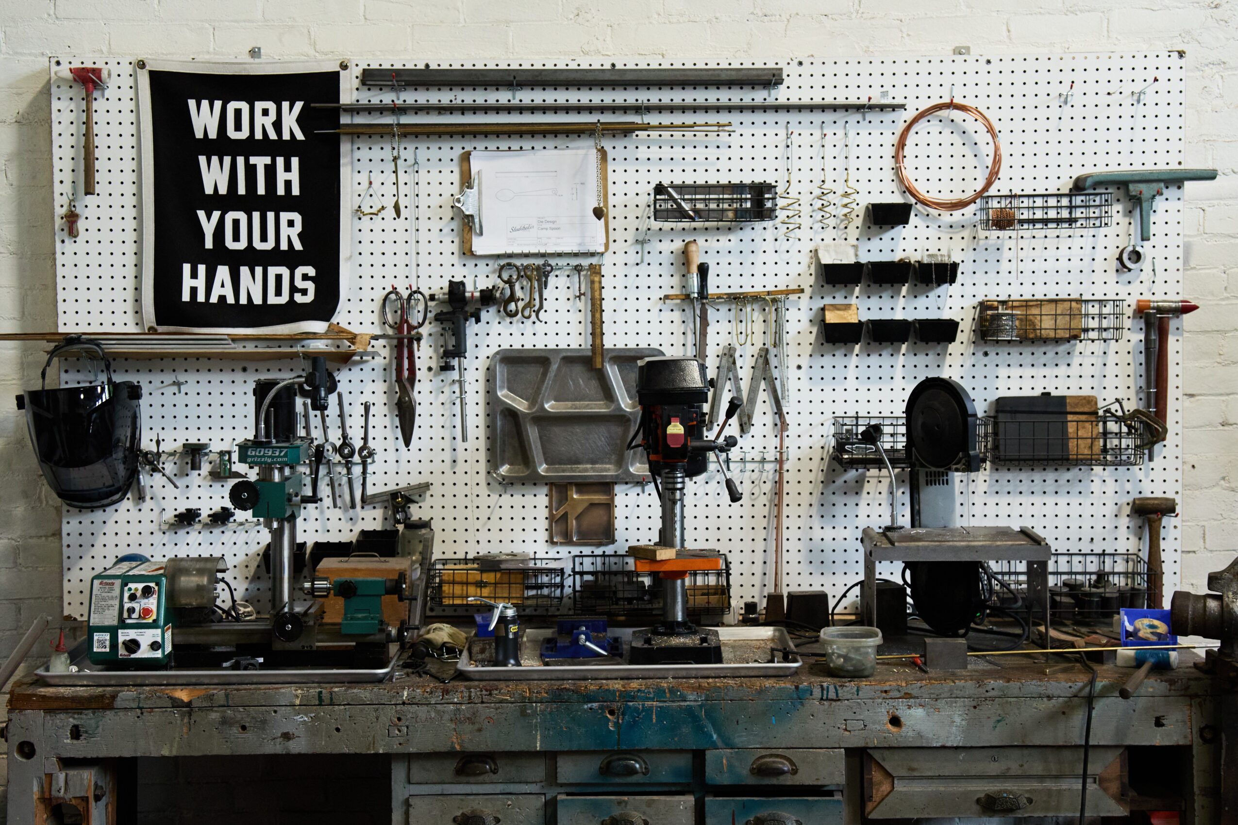 Workshop with tools hanging on a pegboard, workbench, and a sign that reads 'Work with your hands'.