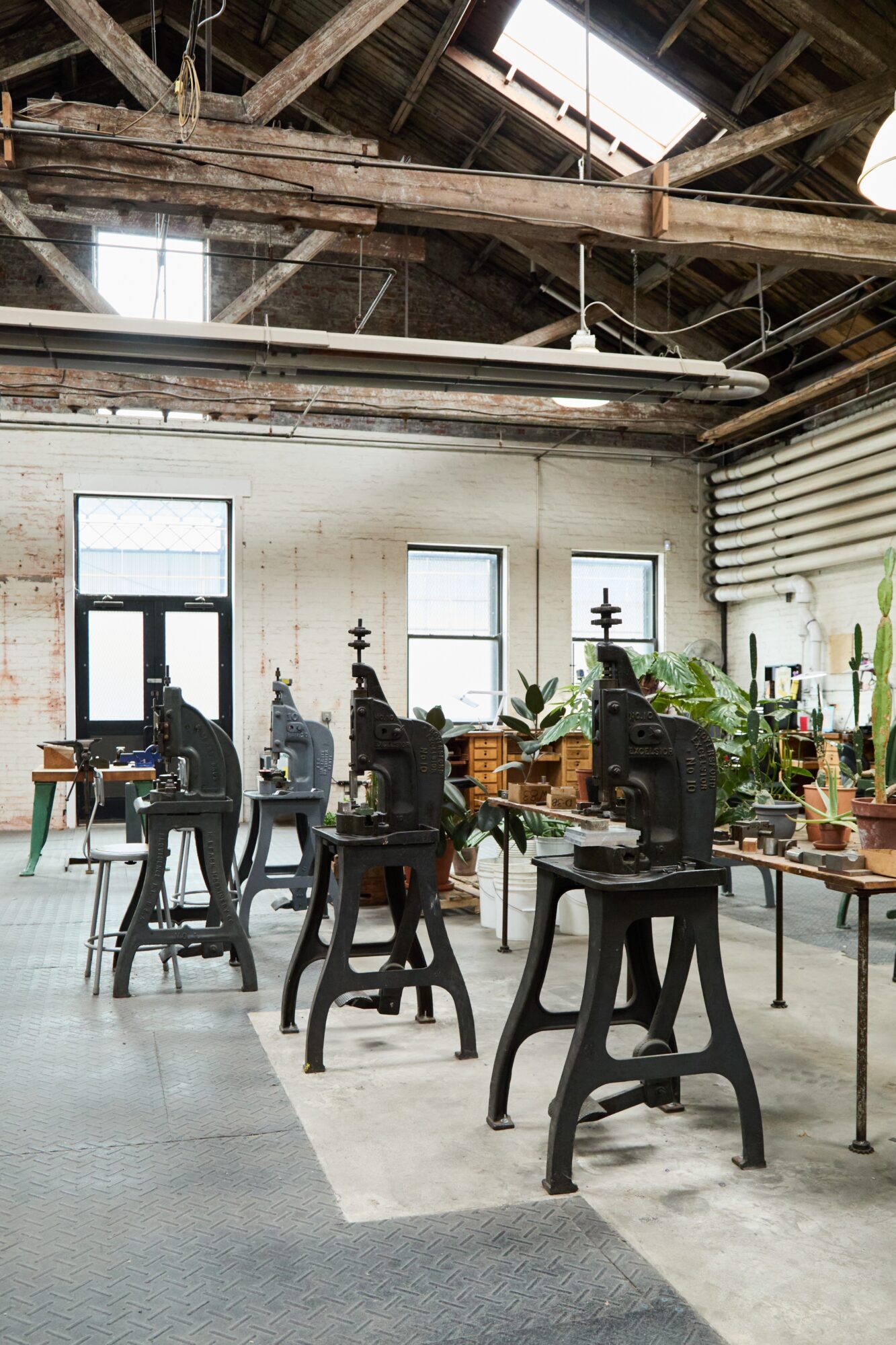 Interior of an industrial-style space with vintage sewing machines on tables, large windows, and exposed wooden beams.