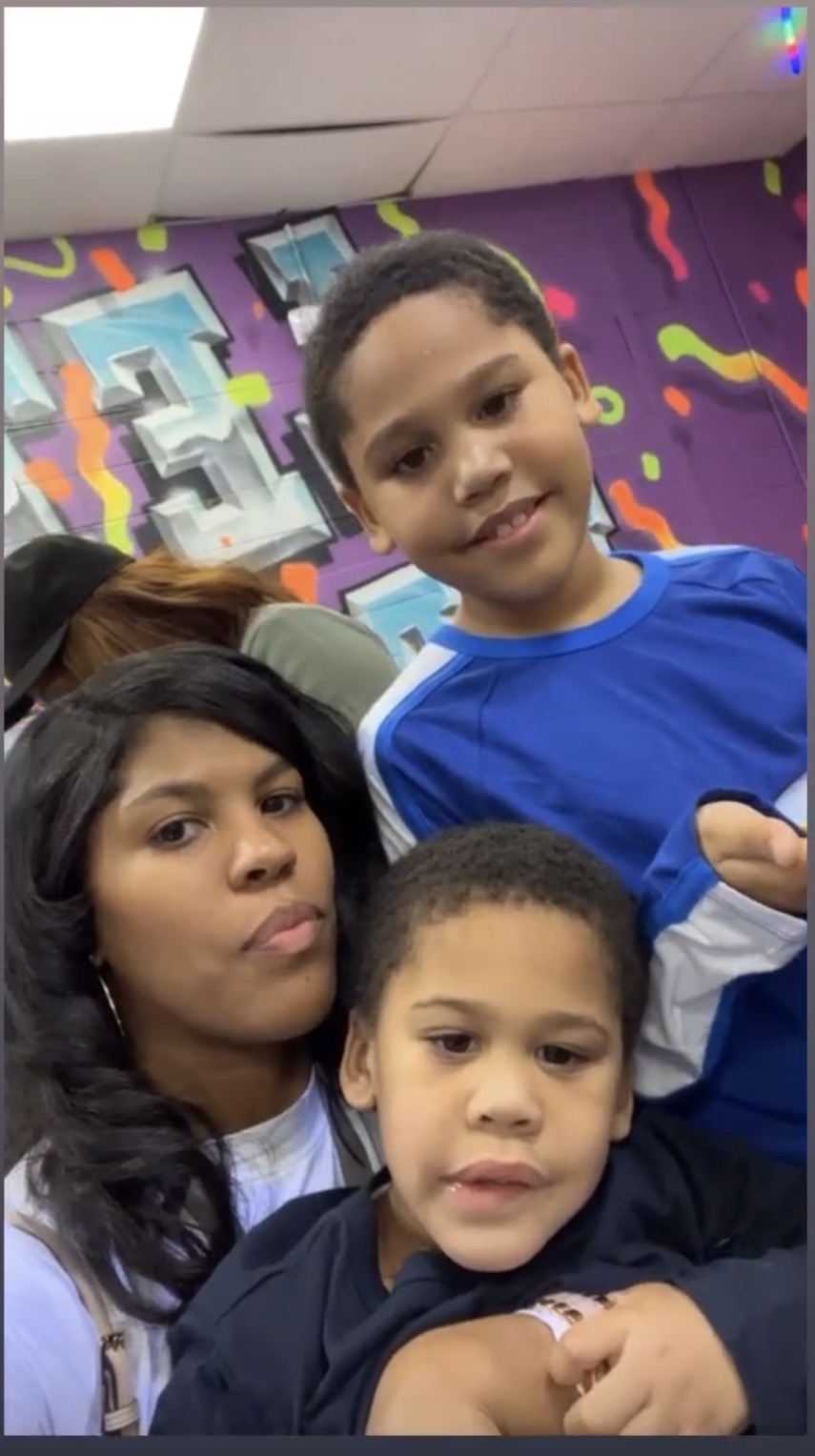 Three children smiling and posing indoors with colorful wall art in the background.