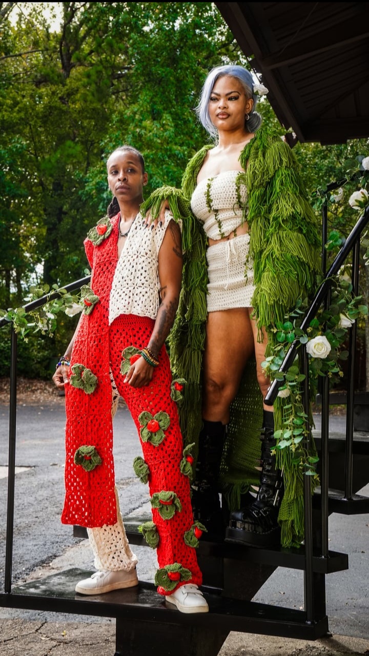 Two women standing on a staircase outdoors, surrounded by greenery, wearing colorful outfits with floral details.