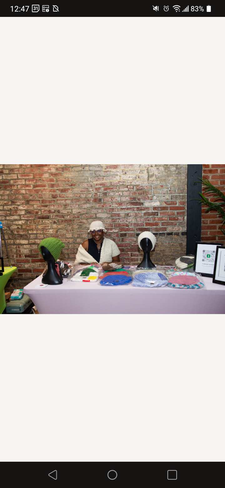 Two people sit behind a table with various items, against a brick wall background.