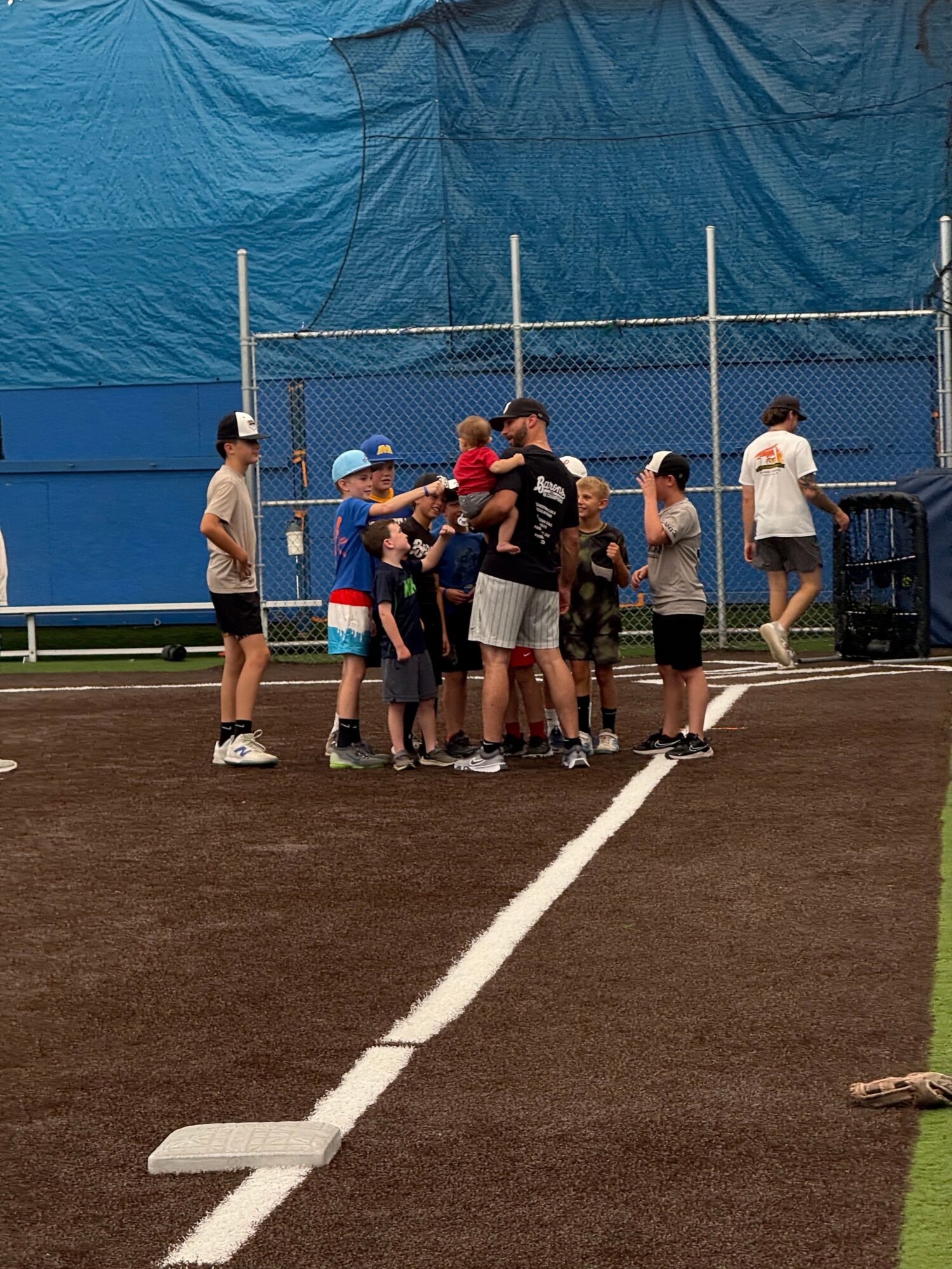 Group of people gathered on a sports field near a blue tent, some holding sports equipment, with a white line on the ground.