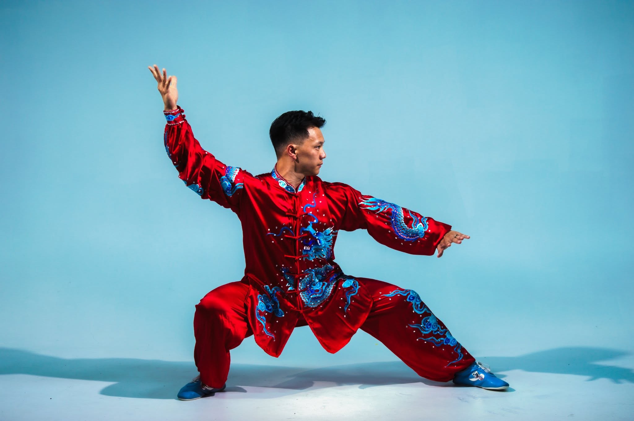 Person in traditional red and blue costume performing a martial arts pose against a blue background.