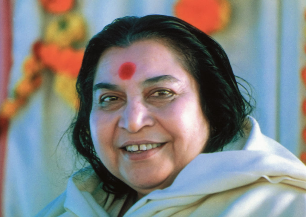 Woman with black hair, smiling, wearing white clothing, with a red mark on her forehead, colorful background.
