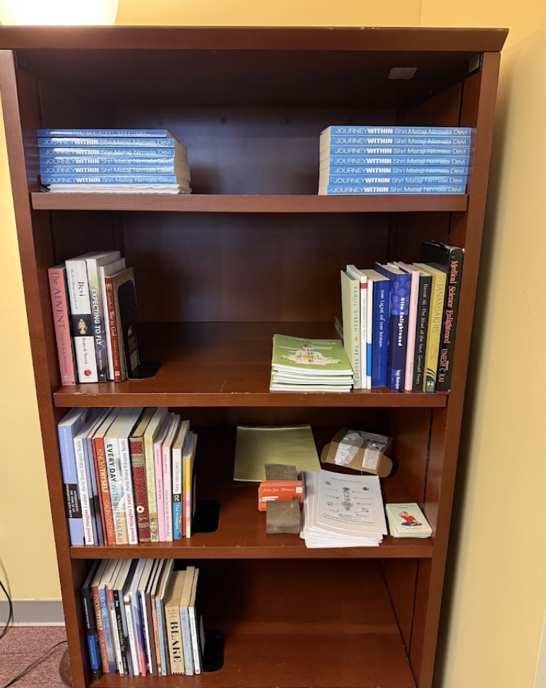 Empty wooden bookshelf with four shelves, some books on the middle shelves, against a yellow wall.