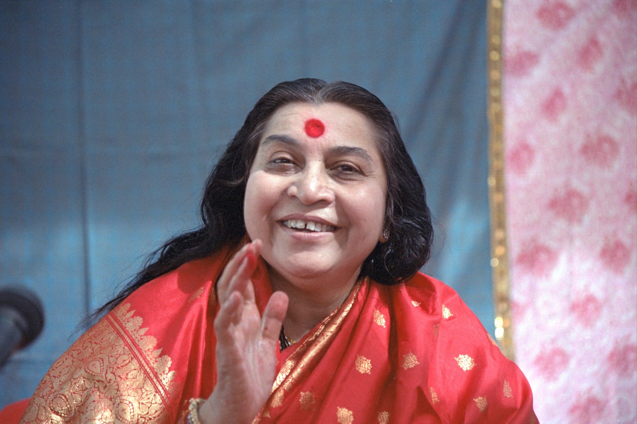 Smiling woman with long dark hair wearing a red and gold traditional outfit, touching her face.