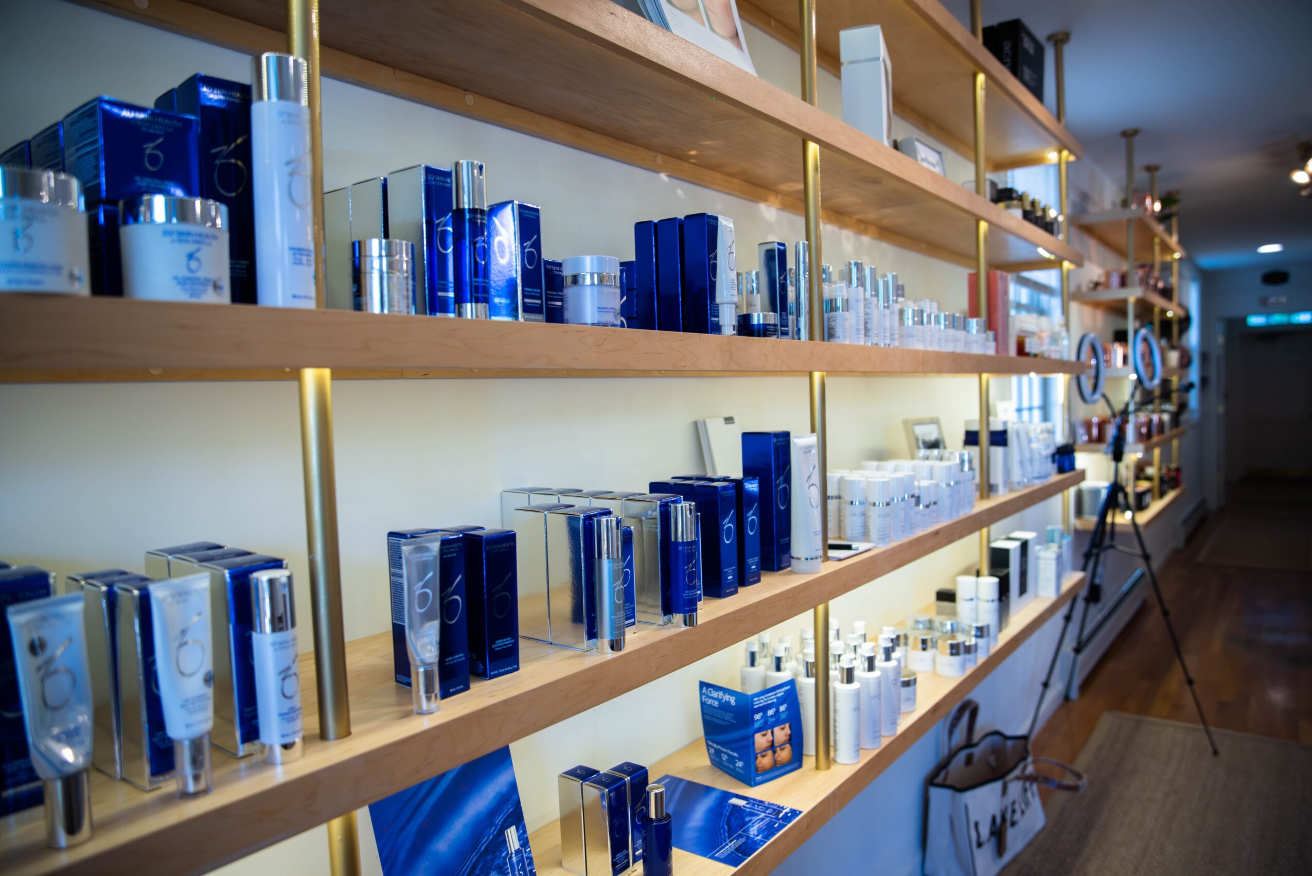 Shelves filled with blue and white skincare products in a store, with a wooden floor and a hallway in the background.