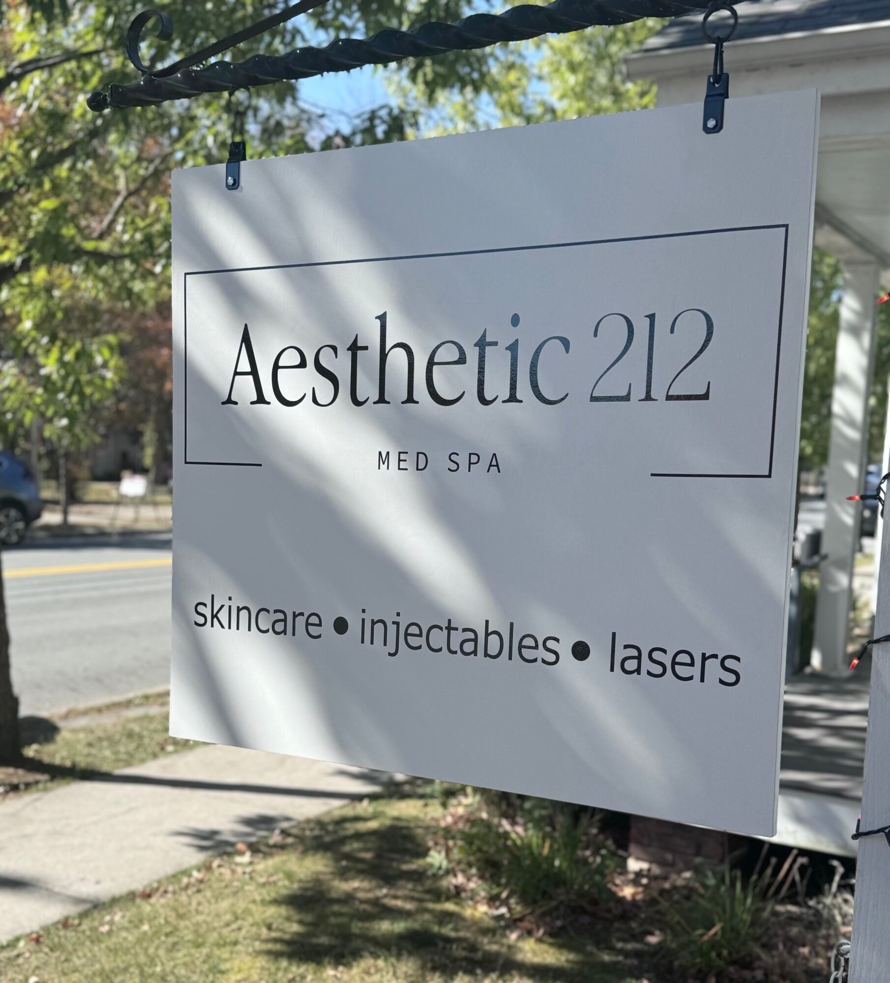Sign for Aesthetic 212 Med Spa with services listed, hanging outdoors on a sunny day.
