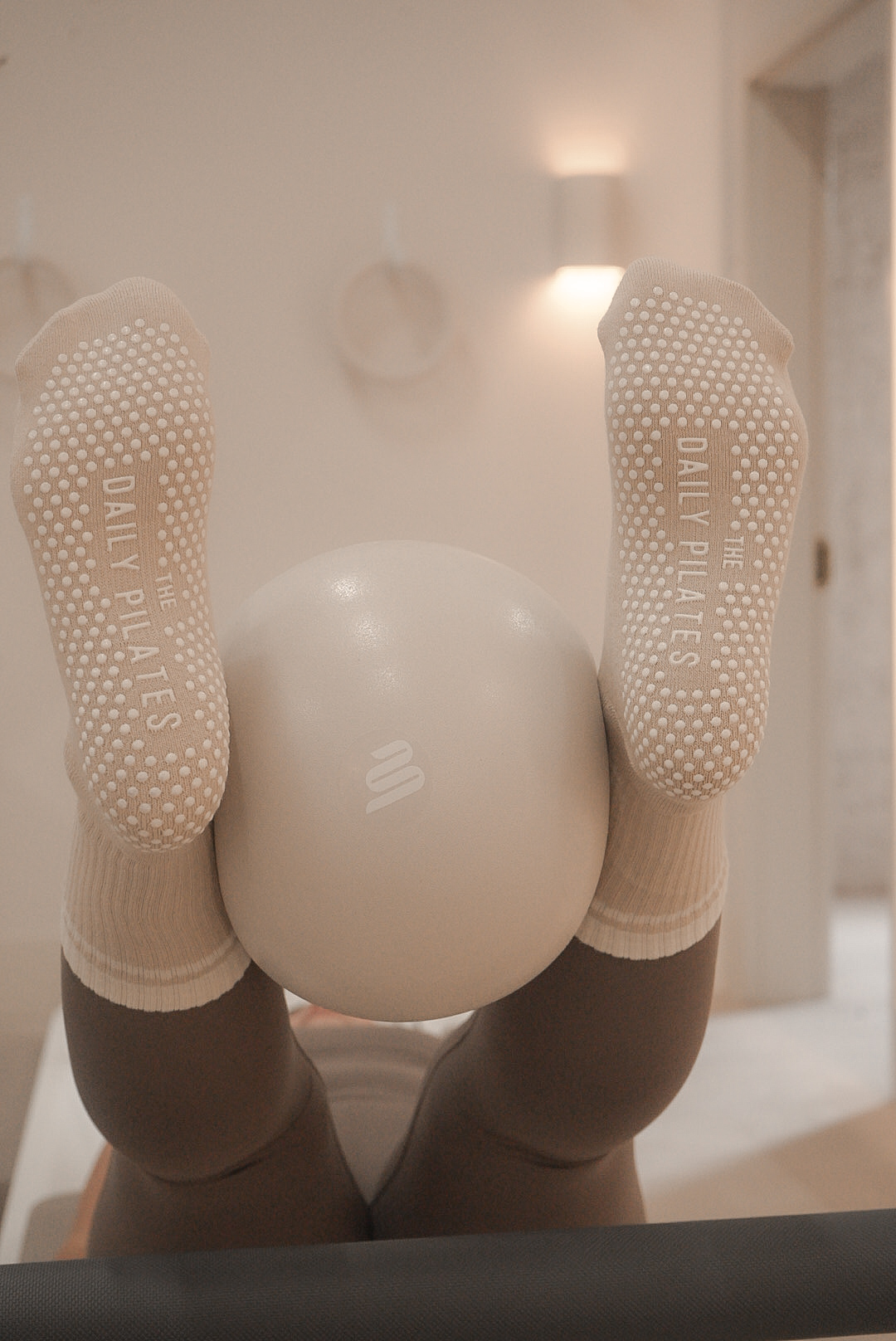 Person holding a white ball with feet in socks visible, upside down view, in a room with wall lights.