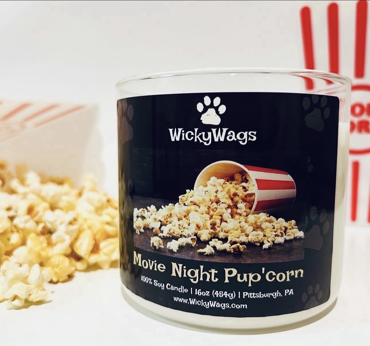 A candle labeled 'Movie Night Popcorn' with popcorn and a popcorn bucket illustration, placed on a surface with popcorn in the background.