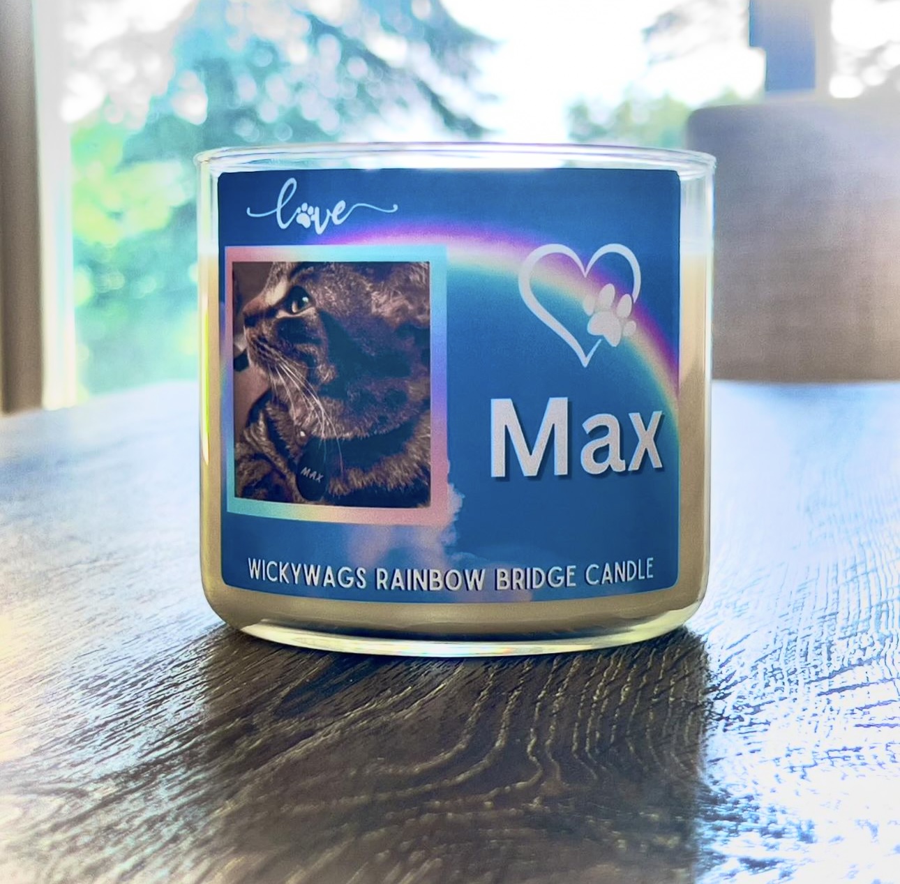 A candle with a label featuring a cat, a rainbow heart, and the name Max, on a wooden table.