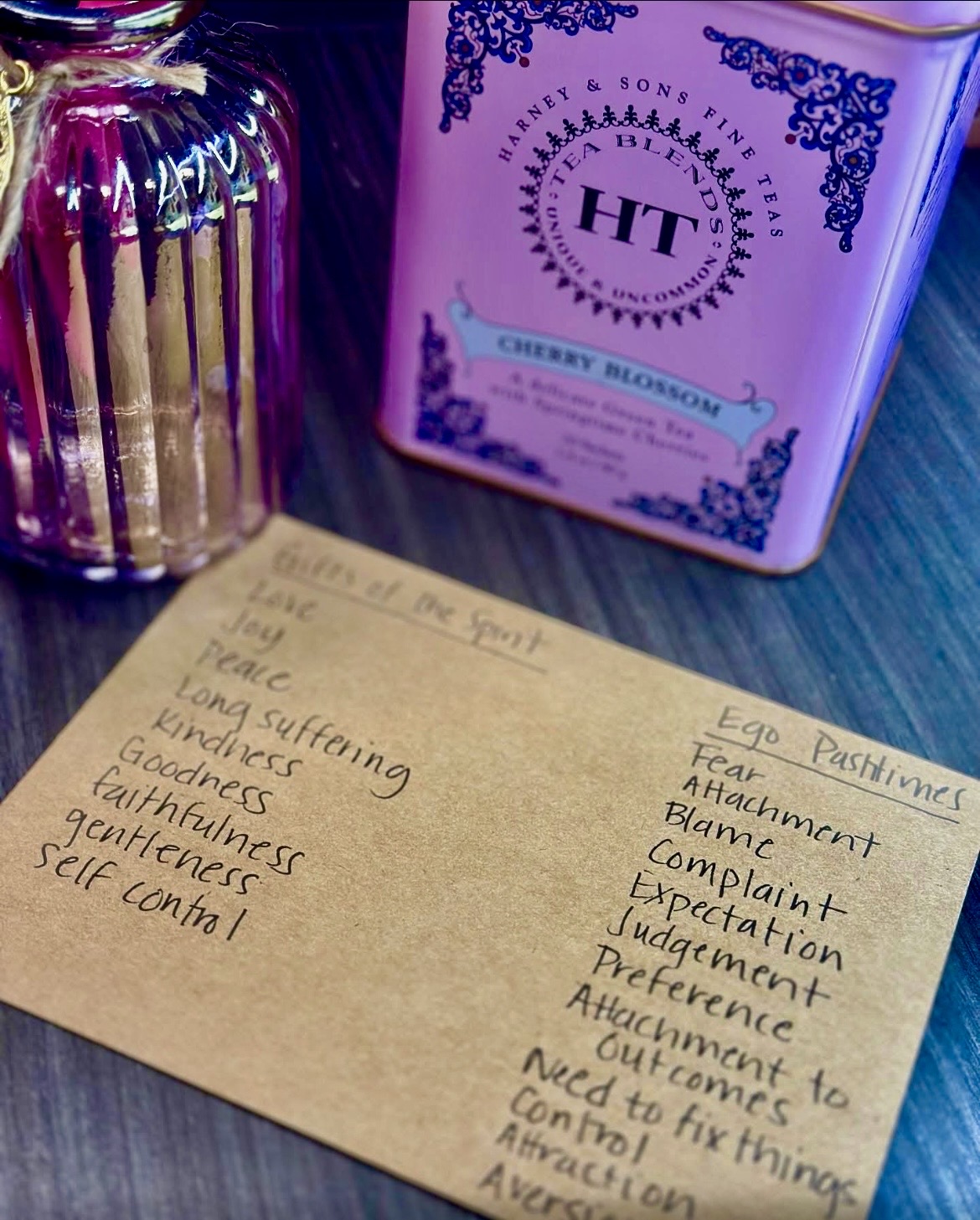 A handwritten list on paper with words like joy, peace, kindness, and fear, placed on a surface near a candle and a box.