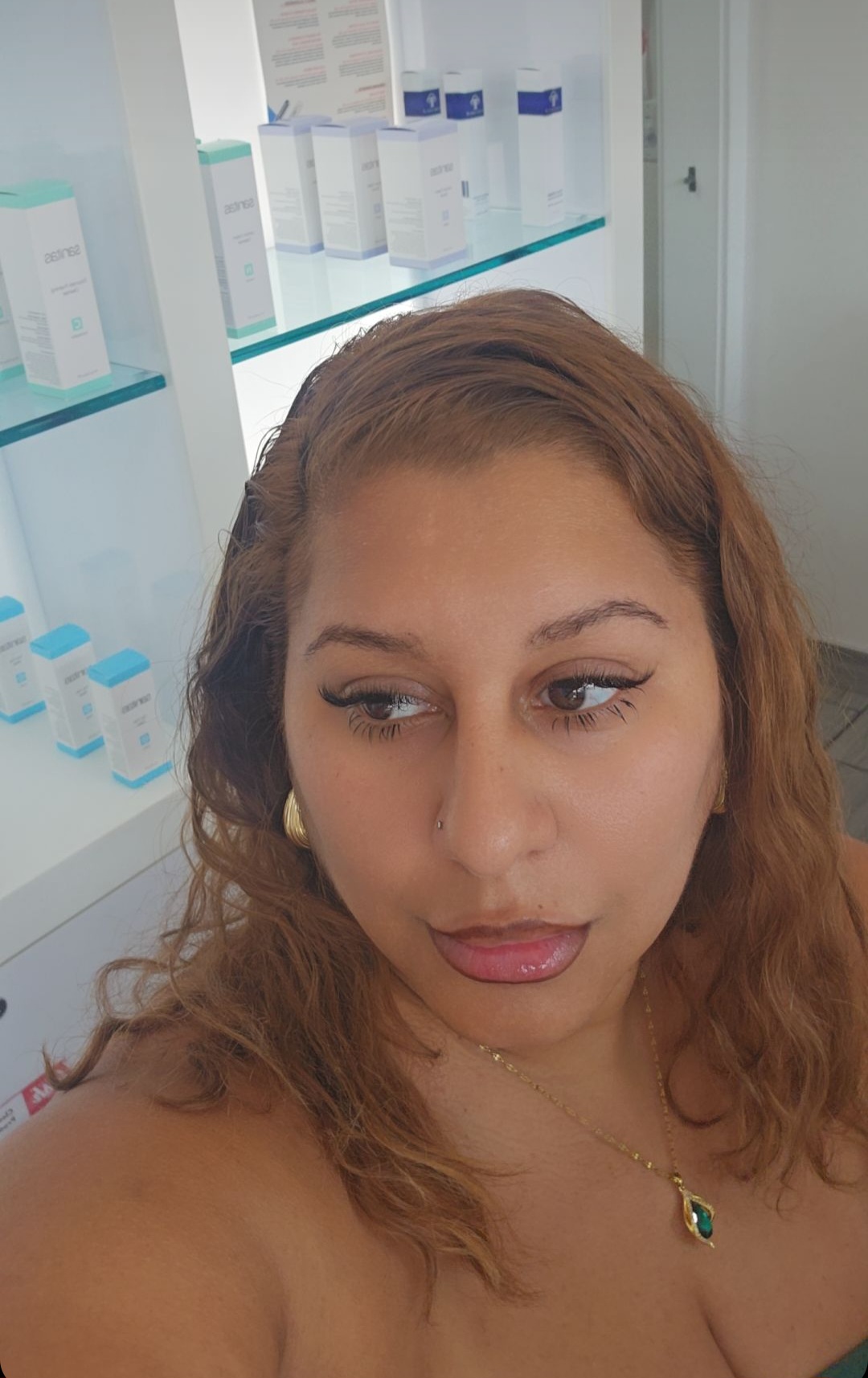 Close-up of a woman with reddish-brown hair looking to the side, in a room with shelves of skincare products.