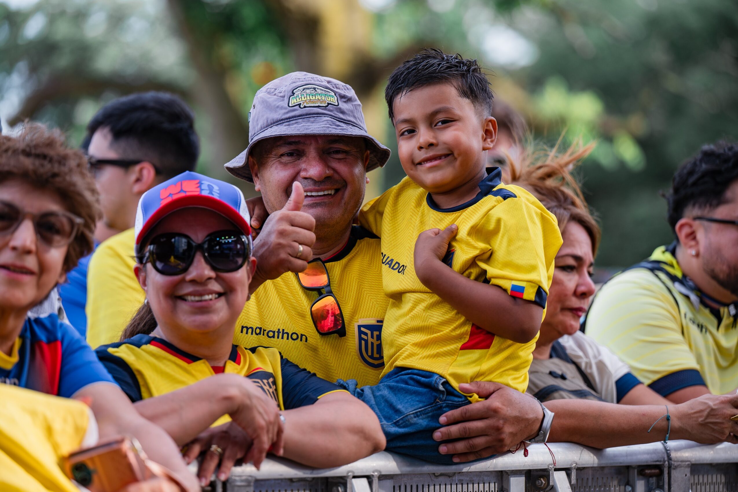 Group of people, including a man and children, smiling and posing outdoors, some wearing yellow sports jerseys.