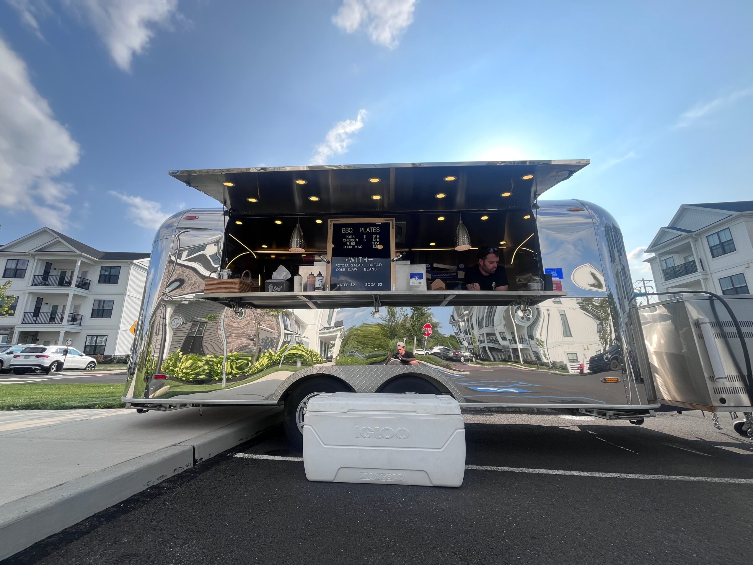 A shiny, modern food truck with a black and silver exterior, parked outdoors with residential buildings in the background.