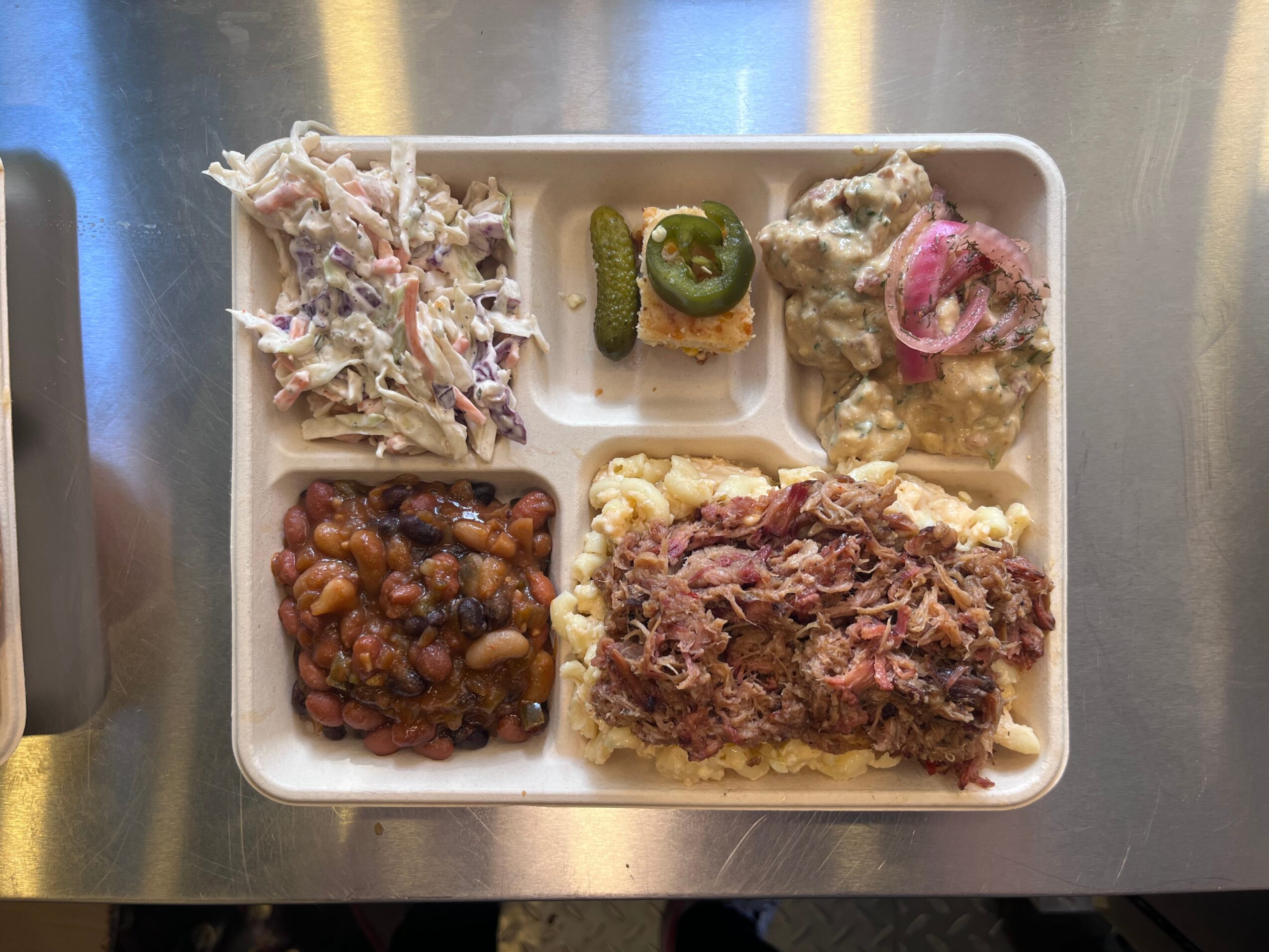 Tray with four food sections: coleslaw, jalapeño and onion, fried item with pink sauce, beans, and ground beef with mashed potatoes