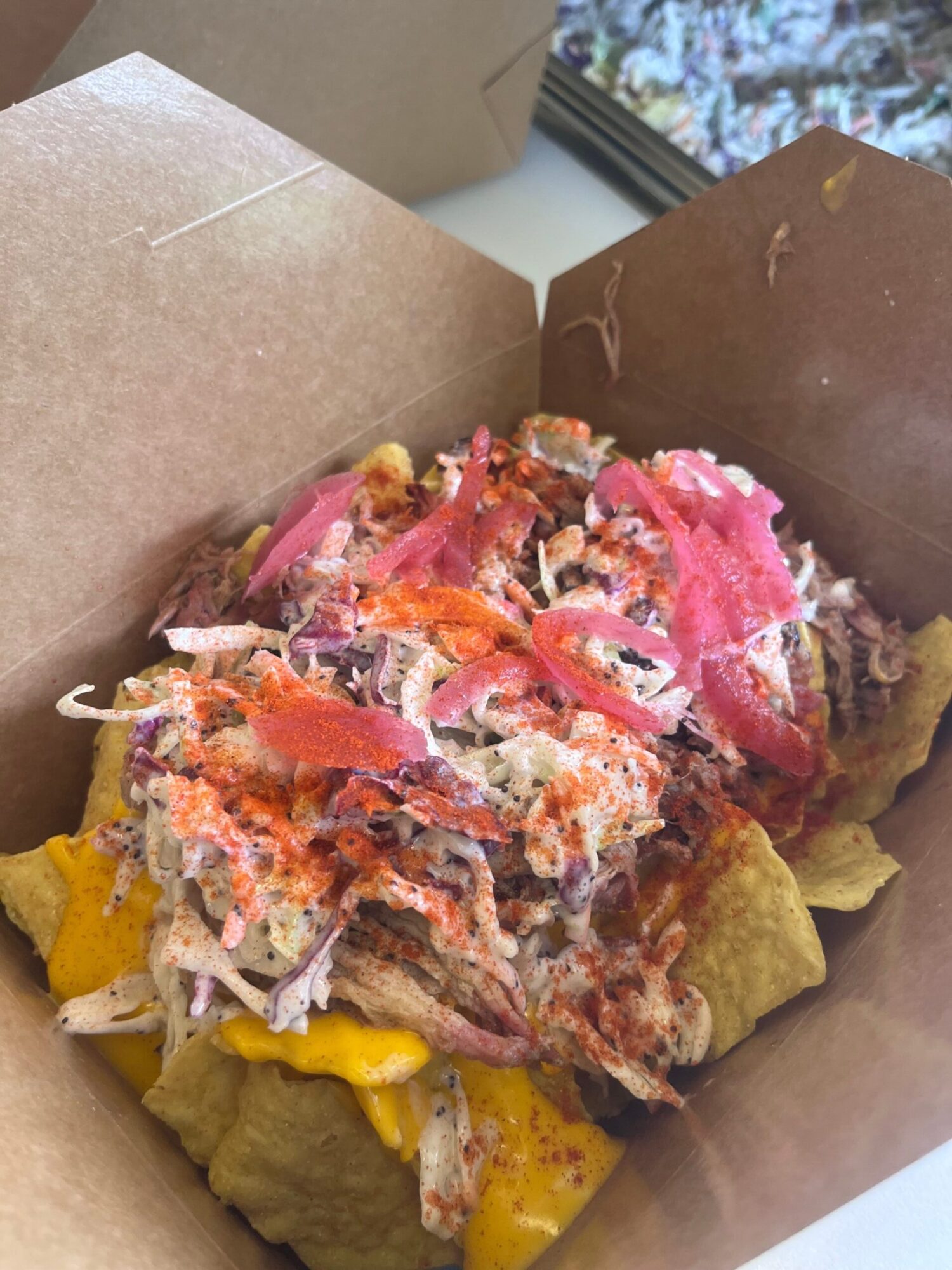 A partially eaten taco with shredded meat, pickled onions, cheese, and lettuce in a paper tray.