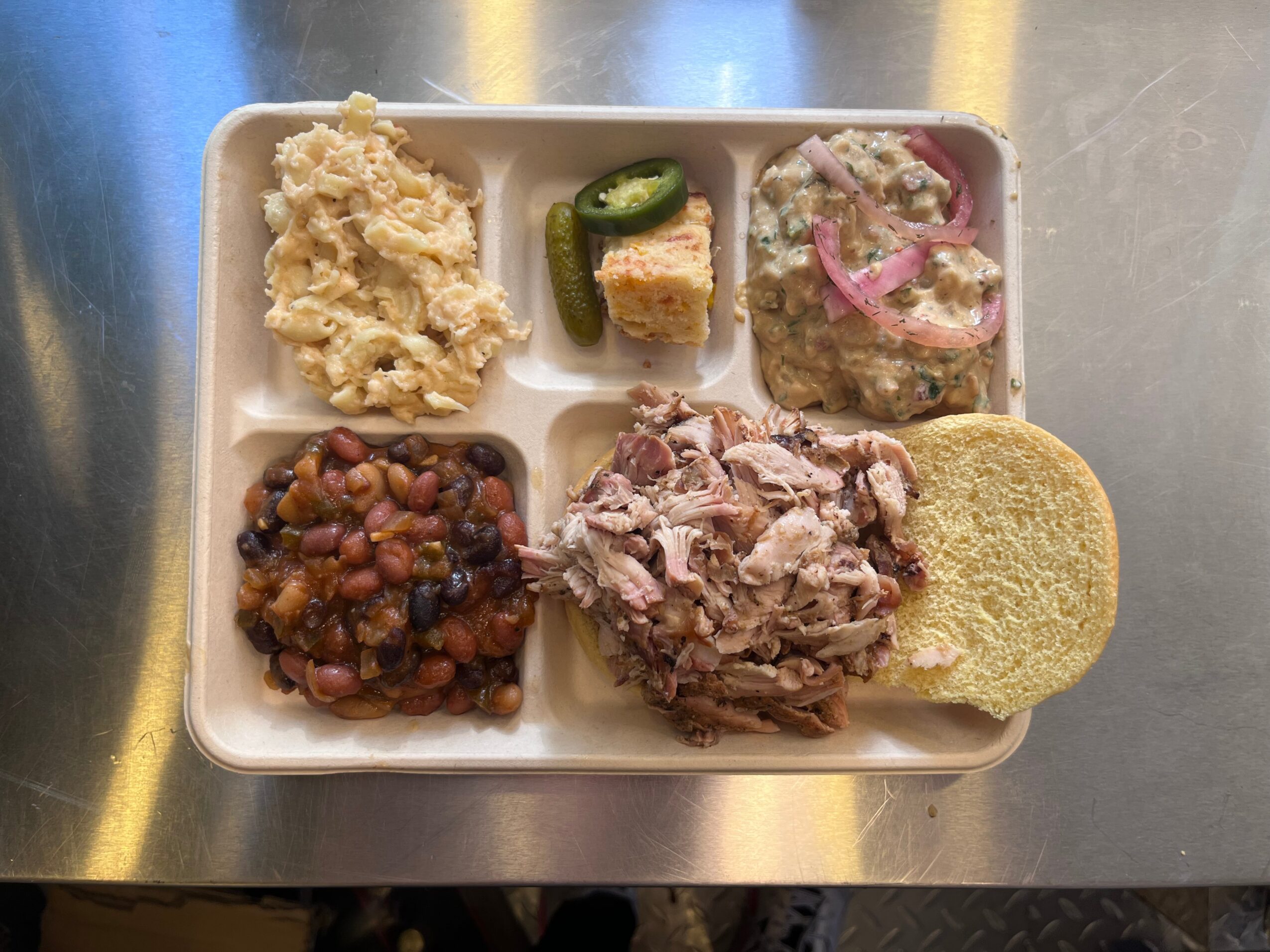 Divided tray with mashed potatoes, cucumber, cornbread, beans, shredded meat, and a biscuit.