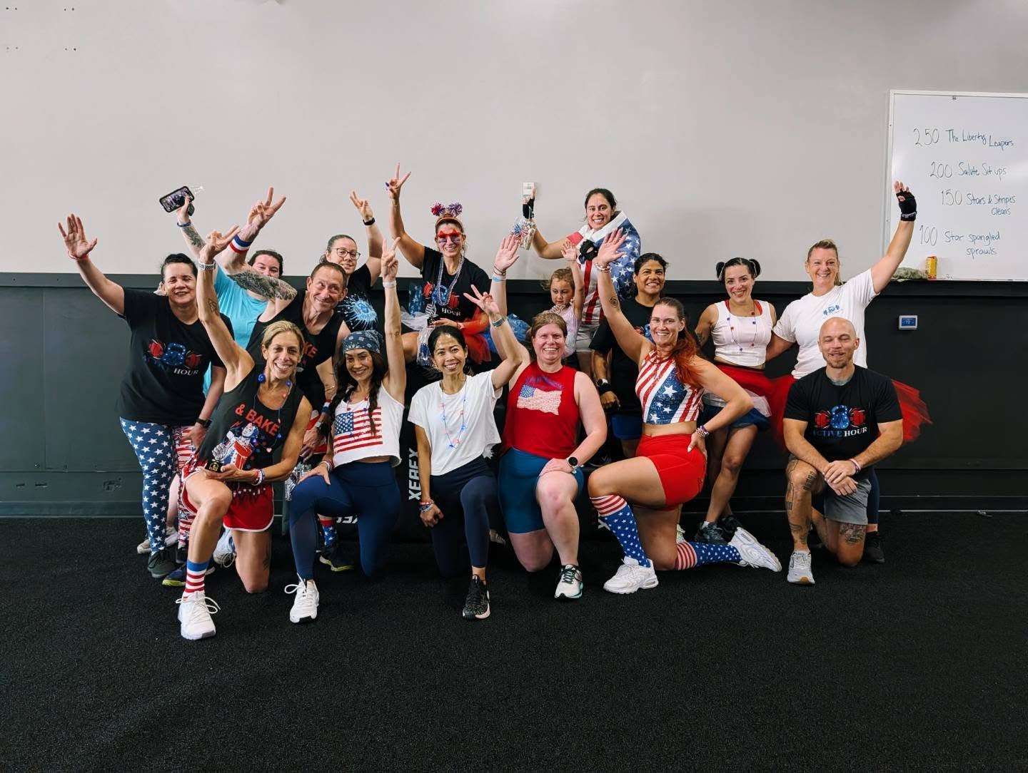 Group of people celebrating, some with arms raised, in a room with a whiteboard, wearing patriotic-themed clothing.