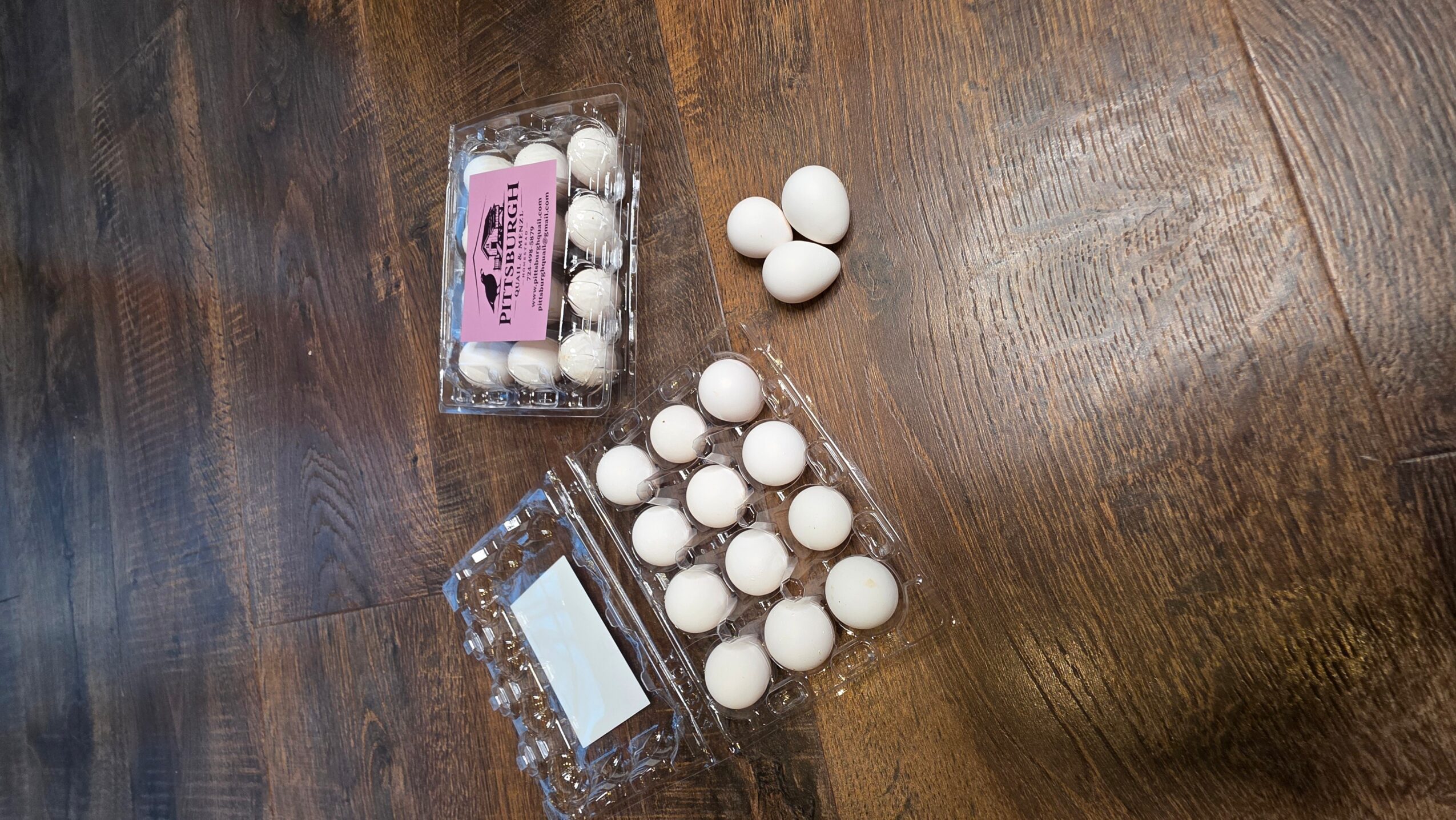 Three containers of white eggs on a wooden surface, with some eggs outside the containers.