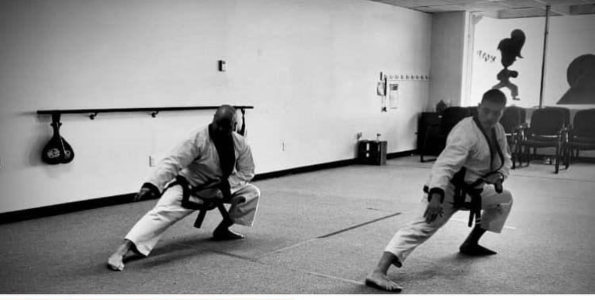 Two people in a martial arts training room, practicing a synchronized move with one person pulling a rope and the other holding a bag.