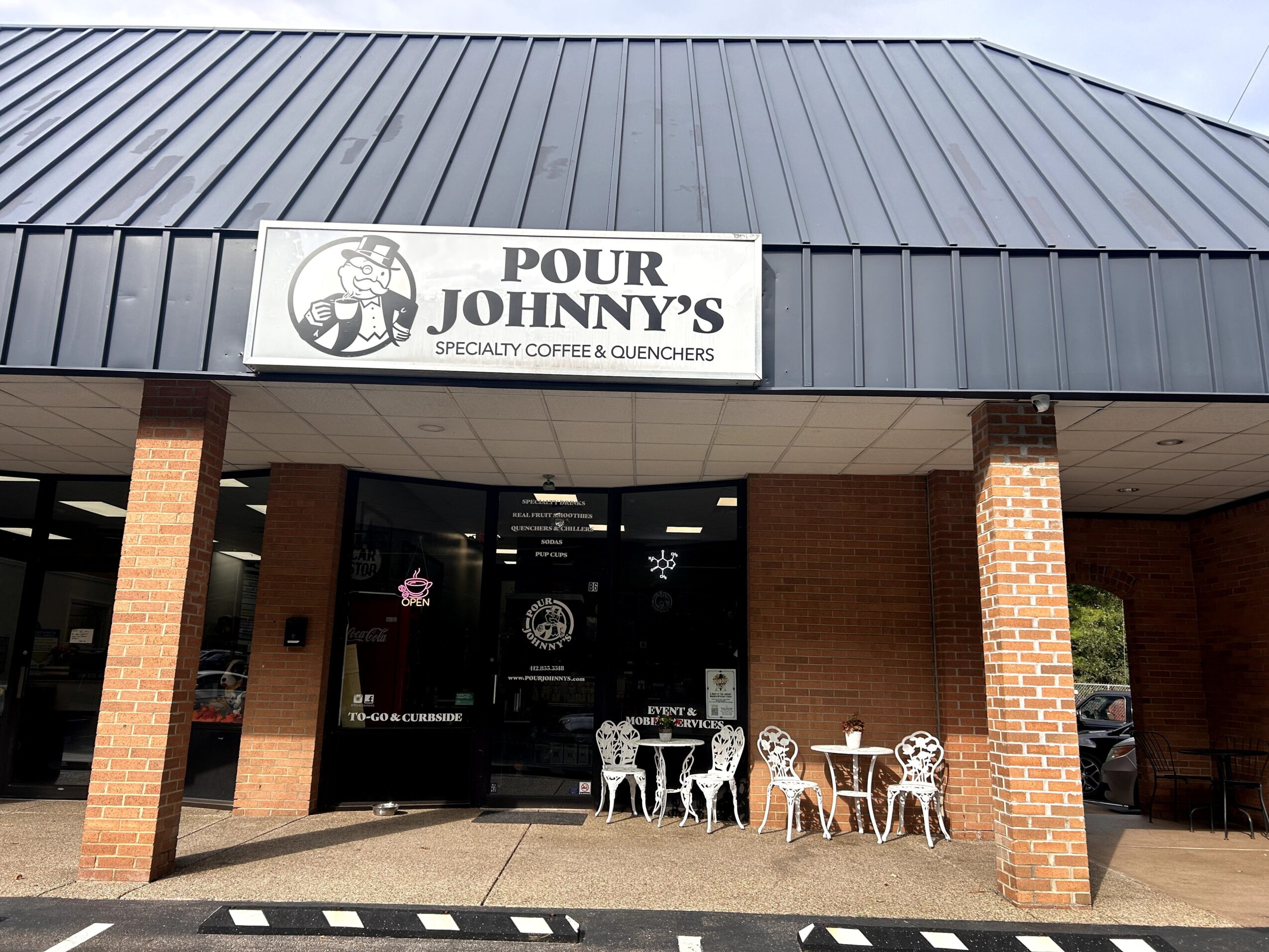 Storefront with a sign reading 'Pour Johnny's' and outdoor seating with white chairs and tables.