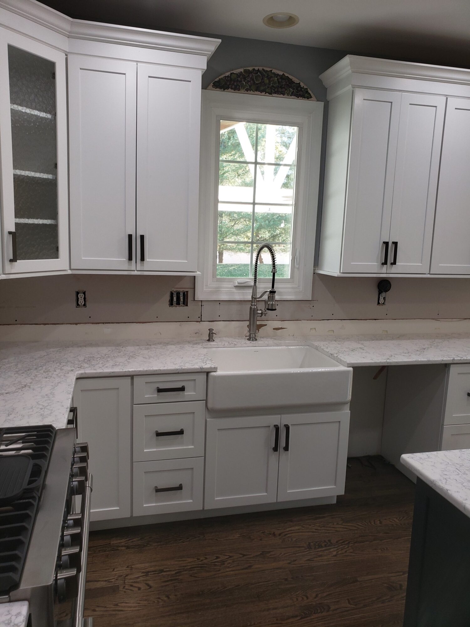 Kitchen with white cabinets, a window above the sink, and a granite countertop, with a stove on the left and dark wood flooring.