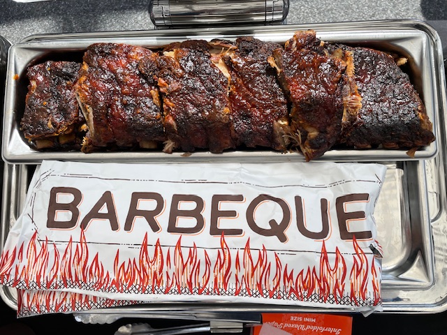 Barbecue ribs on a tray with a paper label reading 'BARBEQUE' and flame illustrations.
