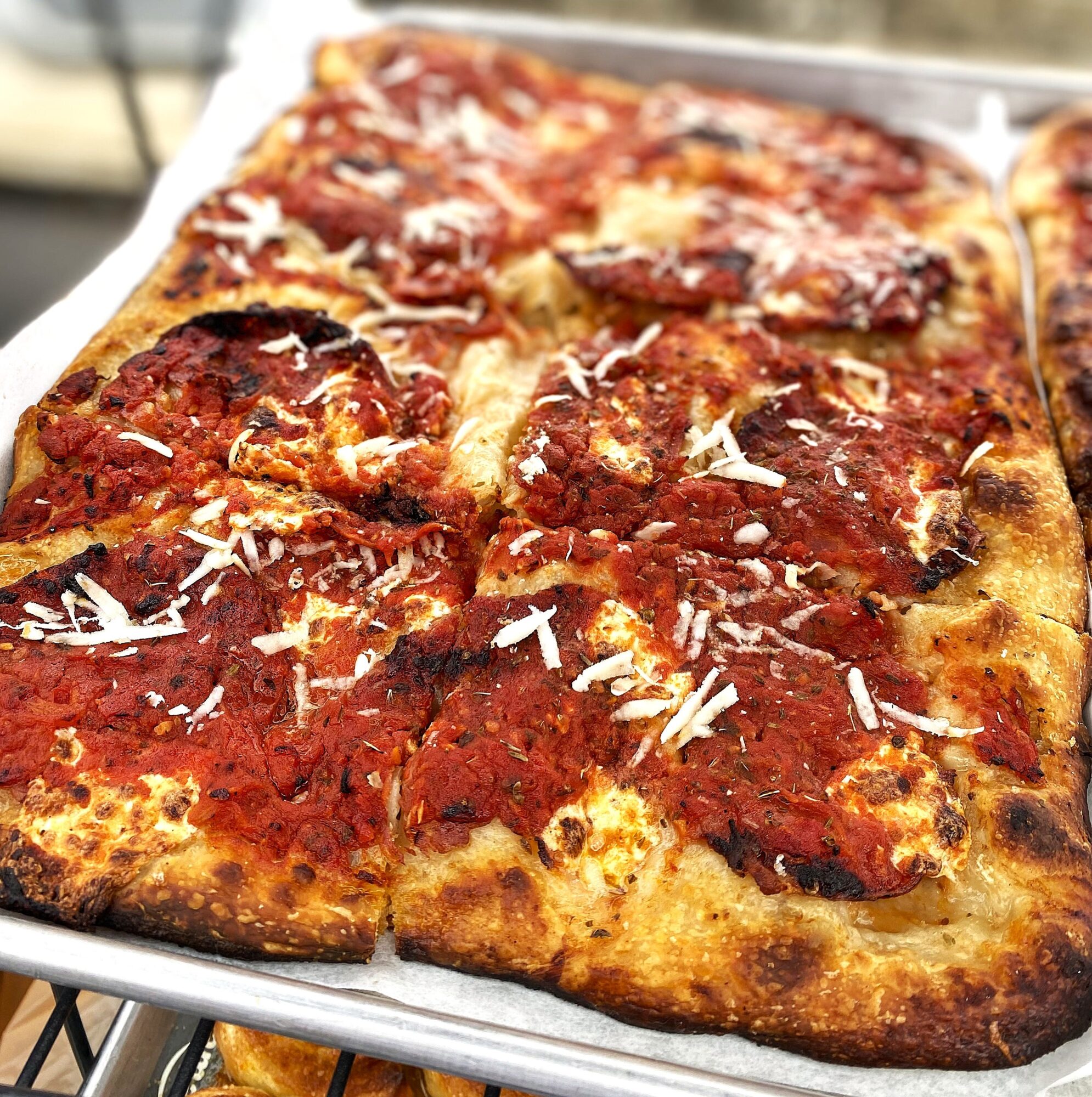 Close-up of a rectangular pizza with pepperoni, cheese, and shredded cheese topping on a metal tray.