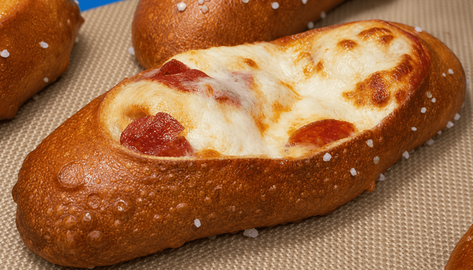 Bread roll filled with melted cheese and pepperoni slices, on a textured surface.