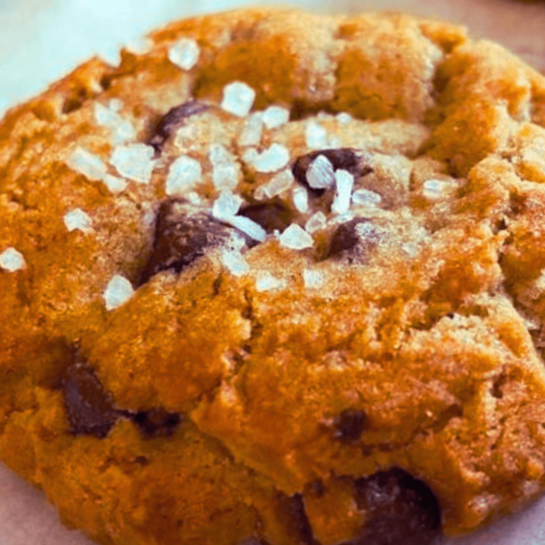 Close-up of a chocolate chip cookie with salt flakes on top, showing a golden-brown crust and chocolate chunks inside.
