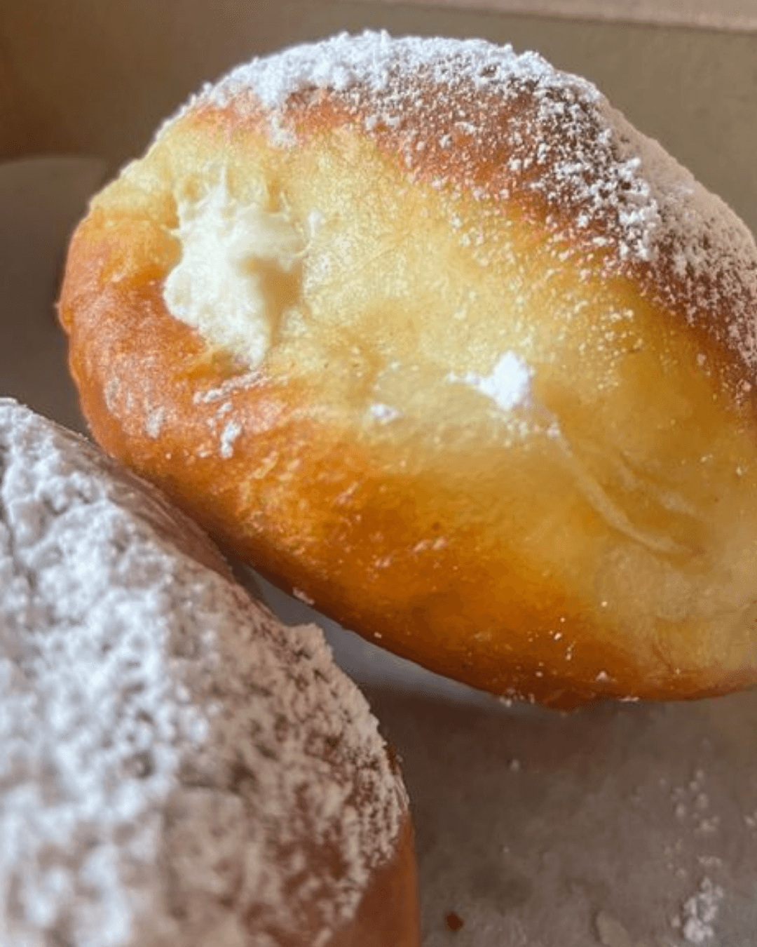 Close-up of a powdered sugar-dusted pastry with a creamy filling visible inside.