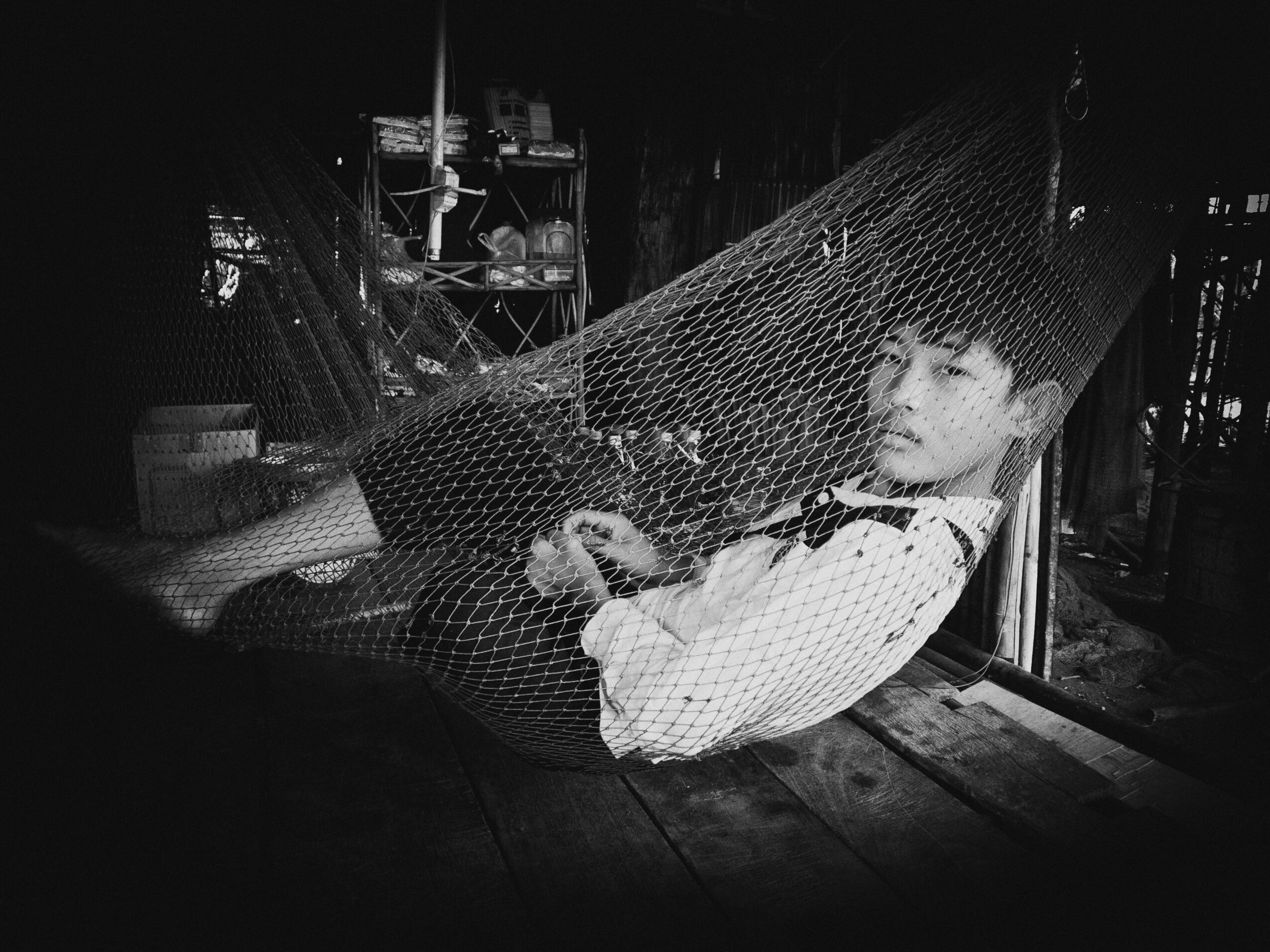 Child lying on a hammock inside a rustic room, surrounded by shelves and wooden furniture.