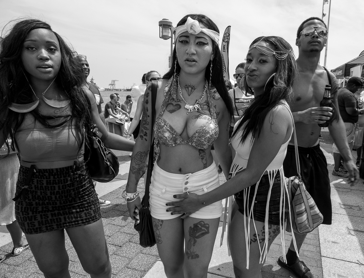 Group of four young women standing outdoors, some with accessories and casual clothing, in a public area.