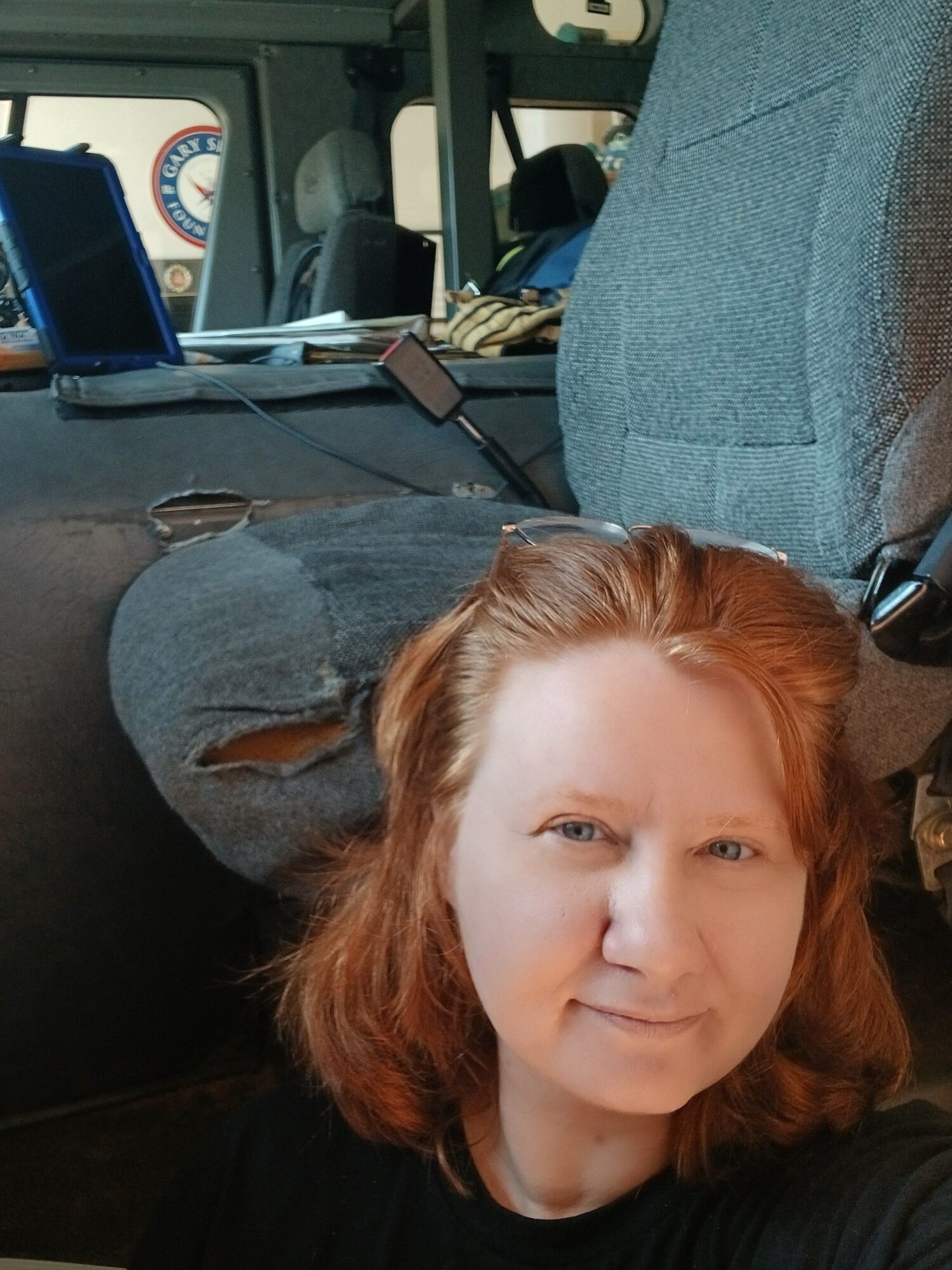 A woman with red hair lying on a seat inside a vehicle, with a gray bag and a window in the background.