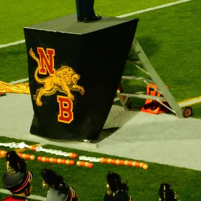 A black podium with a Nebraska logo and a lion, on a sports field, with people in the foreground.