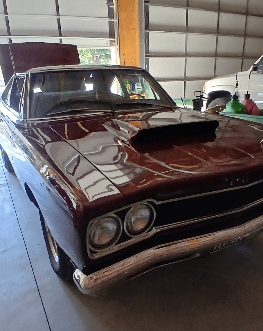 Classic car with a hood scoop, parked inside a garage with a white vehicle in the background.