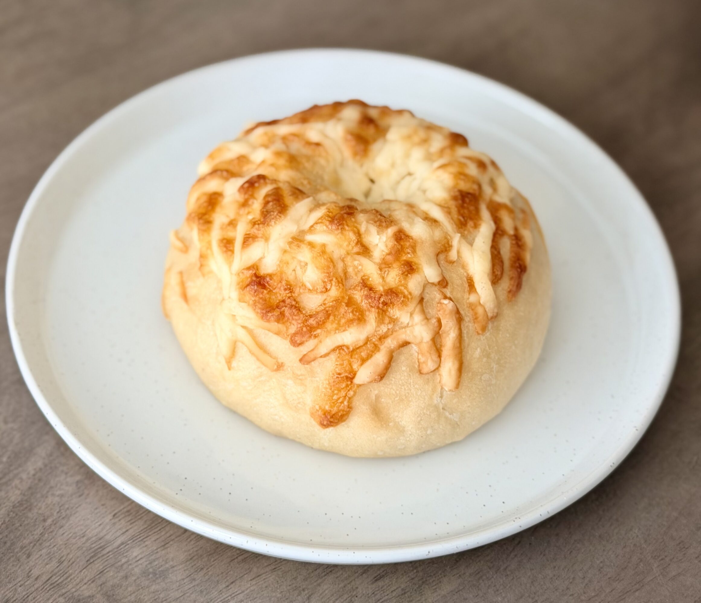 Cheese bread roll on a white plate, with melted cheese on top, placed on a wooden surface.