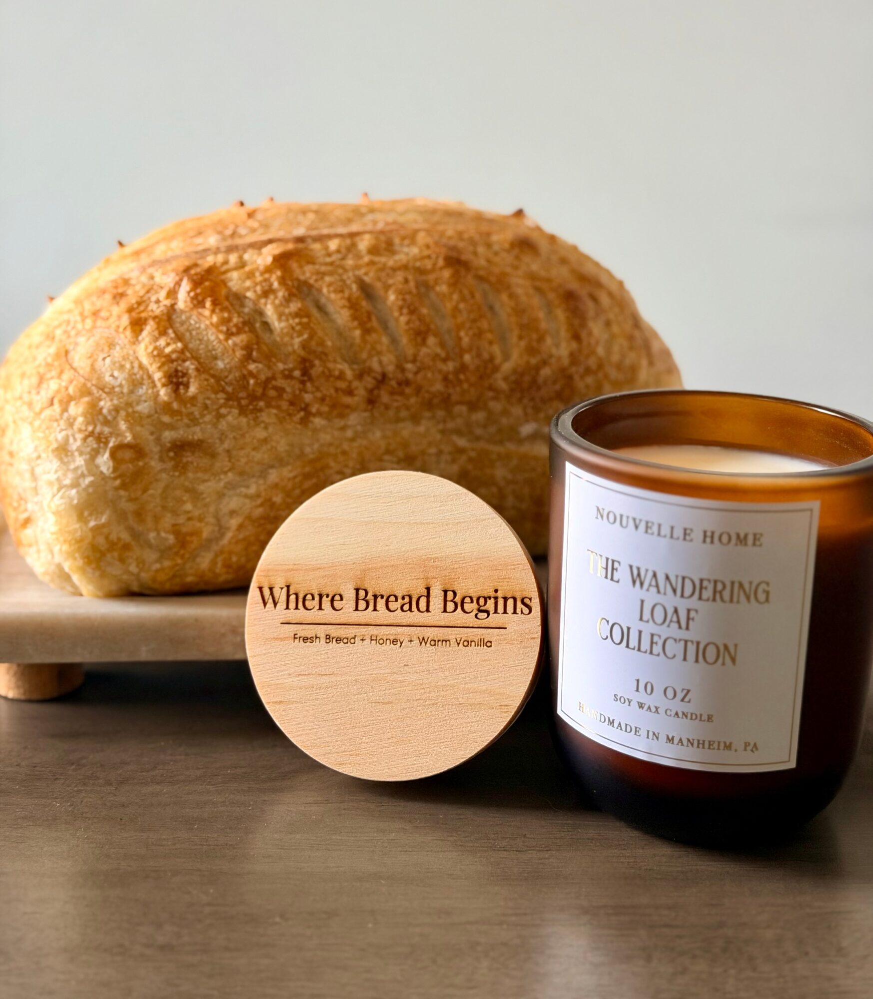 Loaf of bread on a wooden surface with a candle and a round wooden sign reading 'Where Bread Begins'.
