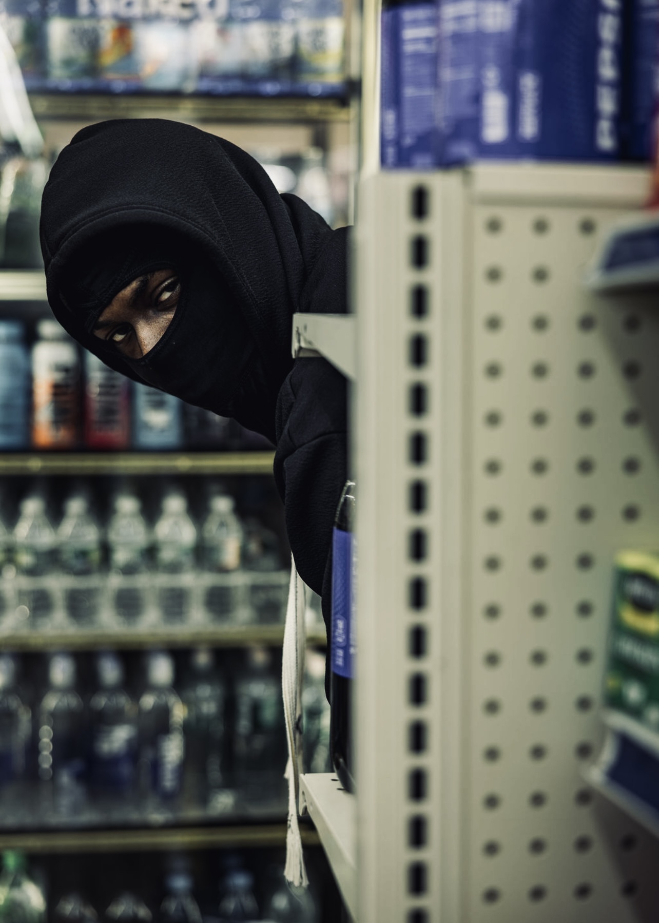 Person wearing a black hijab shopping in a store aisle with shelves of bottled drinks.