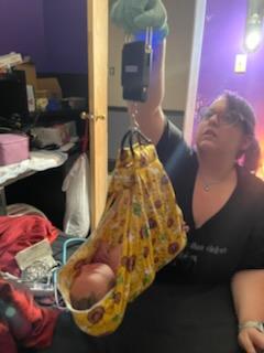 Person taking a selfie with a baby in a yellow floral sling, in a room with purple walls and various objects.