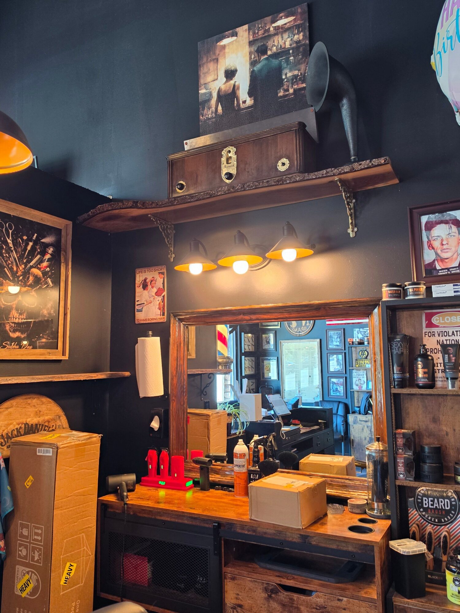 Bar interior with shelves, bottles, and a framed picture, illuminated by warm lighting, with a window in the background.