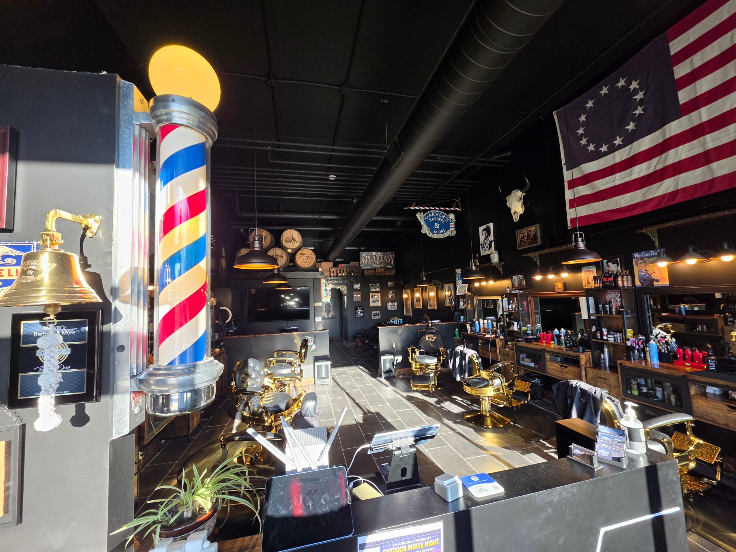 Bar with barber pole, American flag, and bar counter with bottles and glasses, dim lighting, and decorative items.