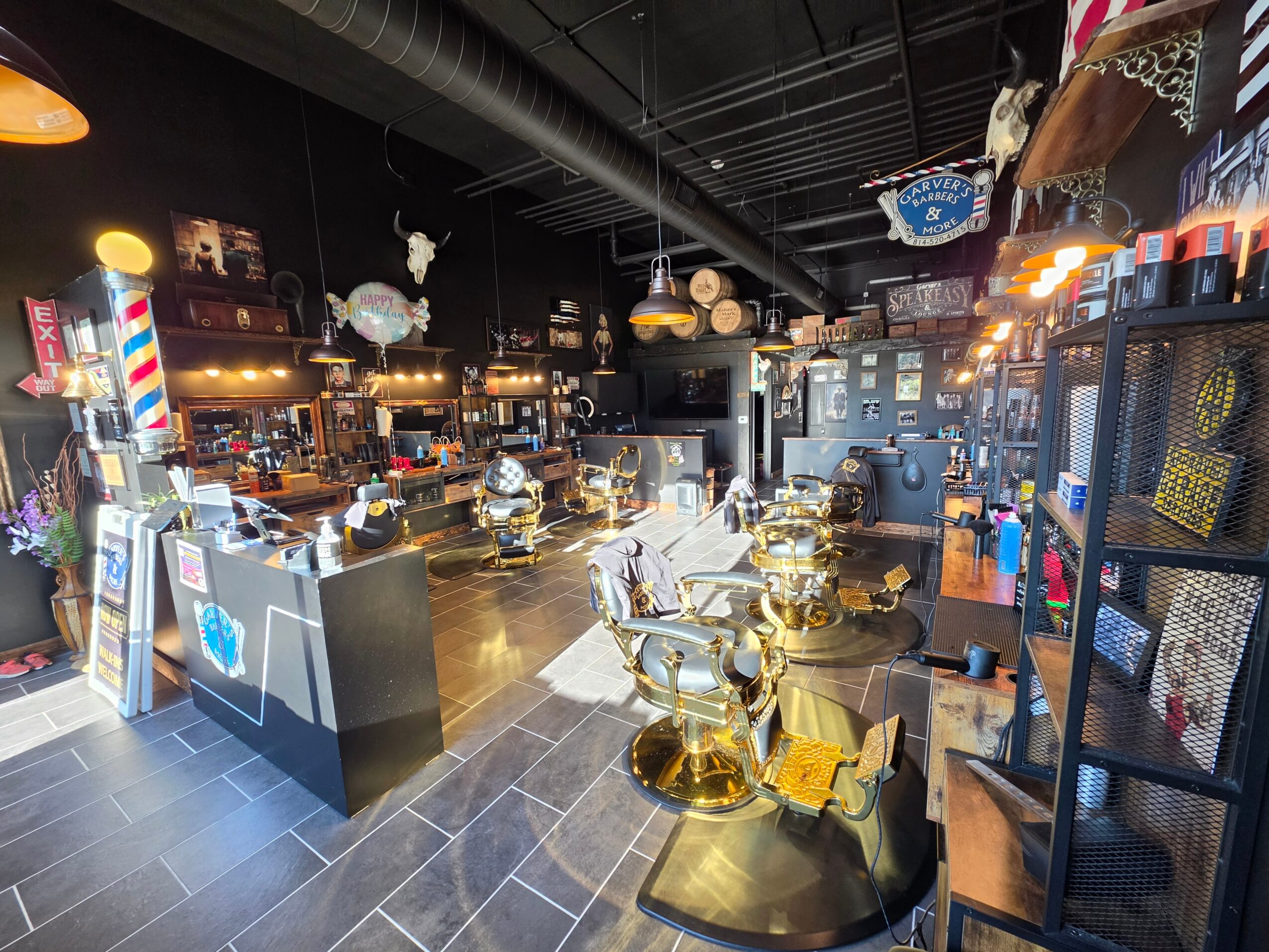 Bar area with gold and black decor, shelves with bottles, and seating, illuminated by warm hanging lights.