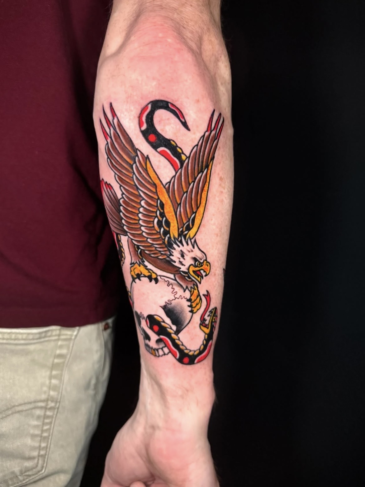 Colorful tattoo of a bird with outstretched wings and a snake intertwined, on a person's forearm.