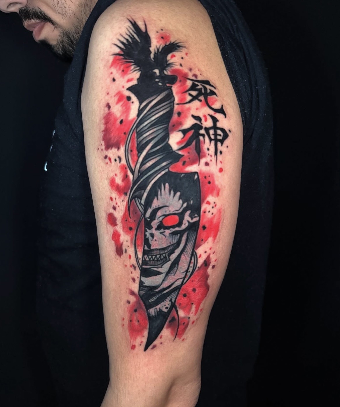 Tattoo of a skull with a sword and Japanese characters on a person's upper arm, with red ink splashes background.