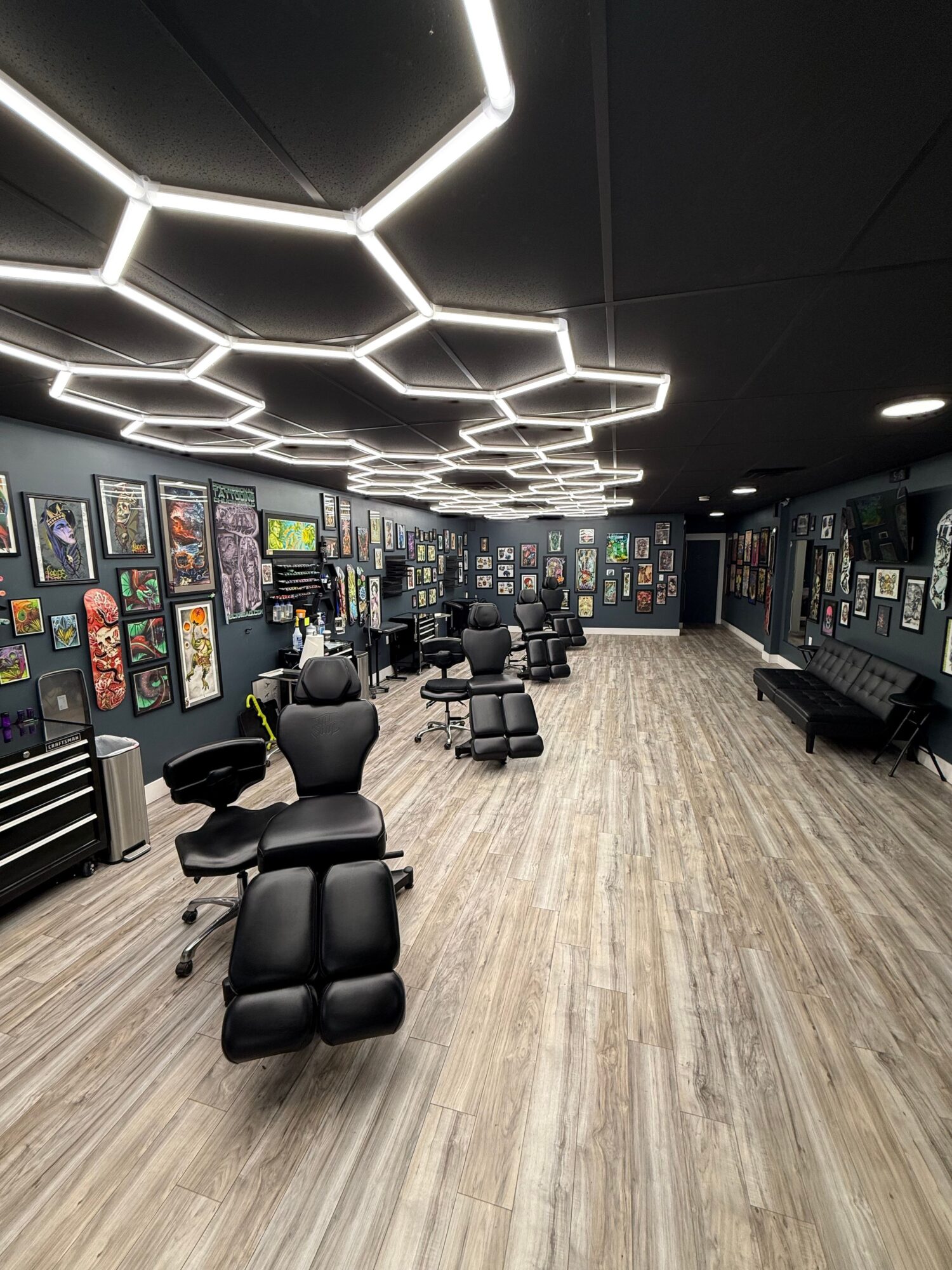 Office with black walls, hexagonal ceiling lights, wooden floor, and multiple chairs and desks, with artwork on walls.