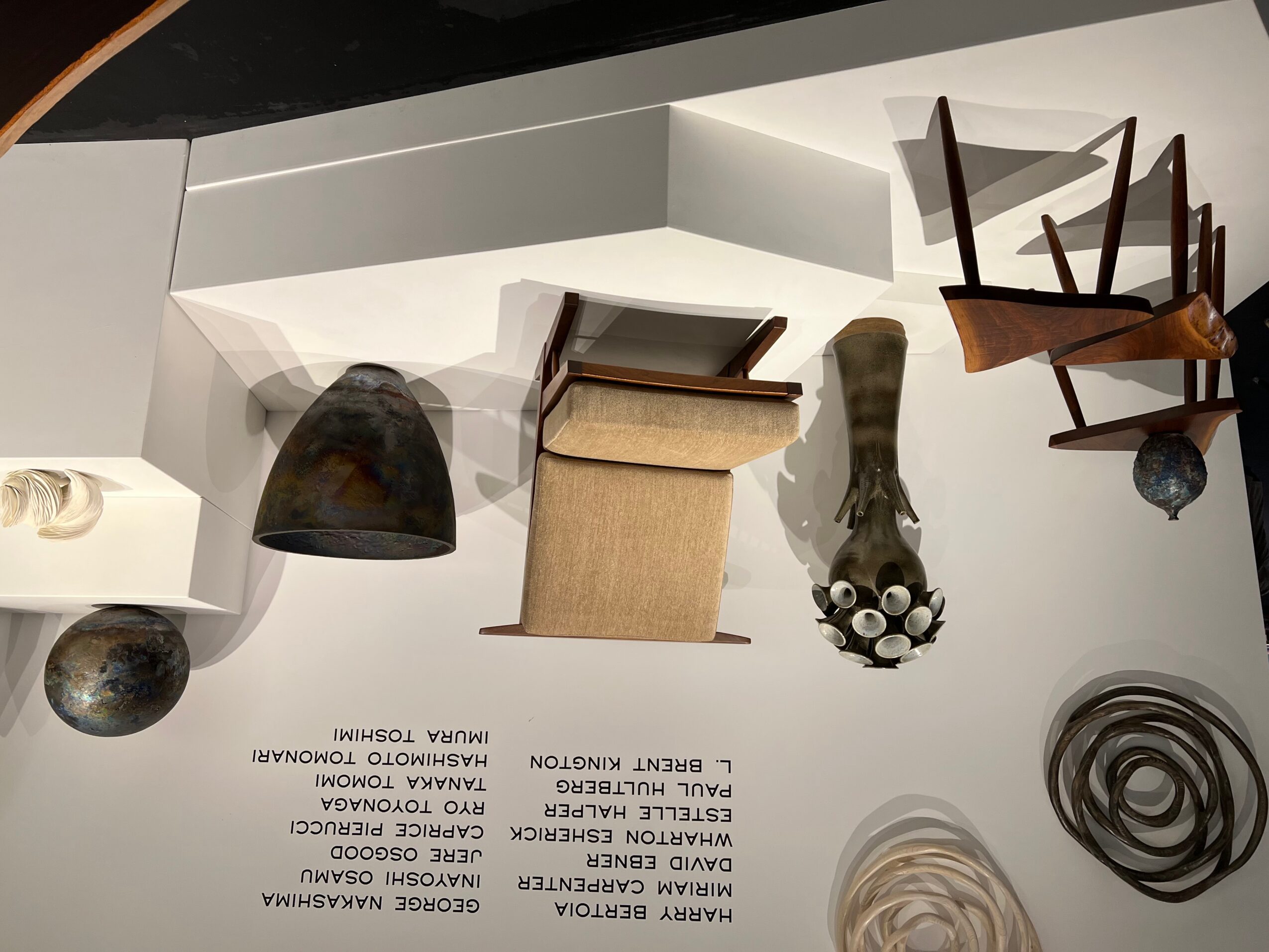 Various chairs and decorative objects on a white surface, with some chairs stacked and a black lamp. Alt text word count: 20.