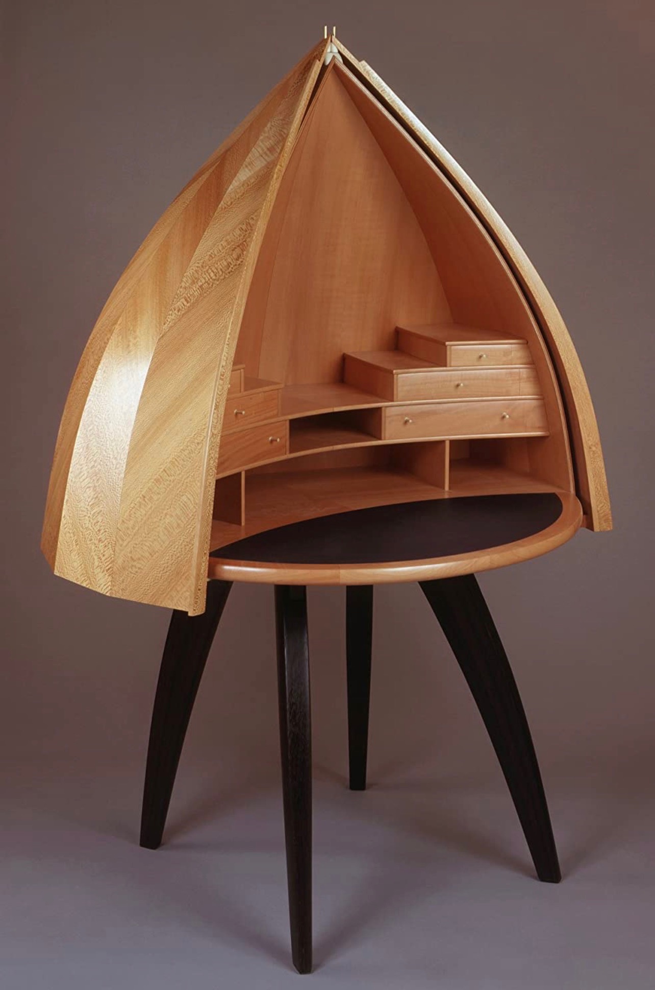 Wooden boat-shaped display case with shelves and drawers on a black stand, against a plain background.