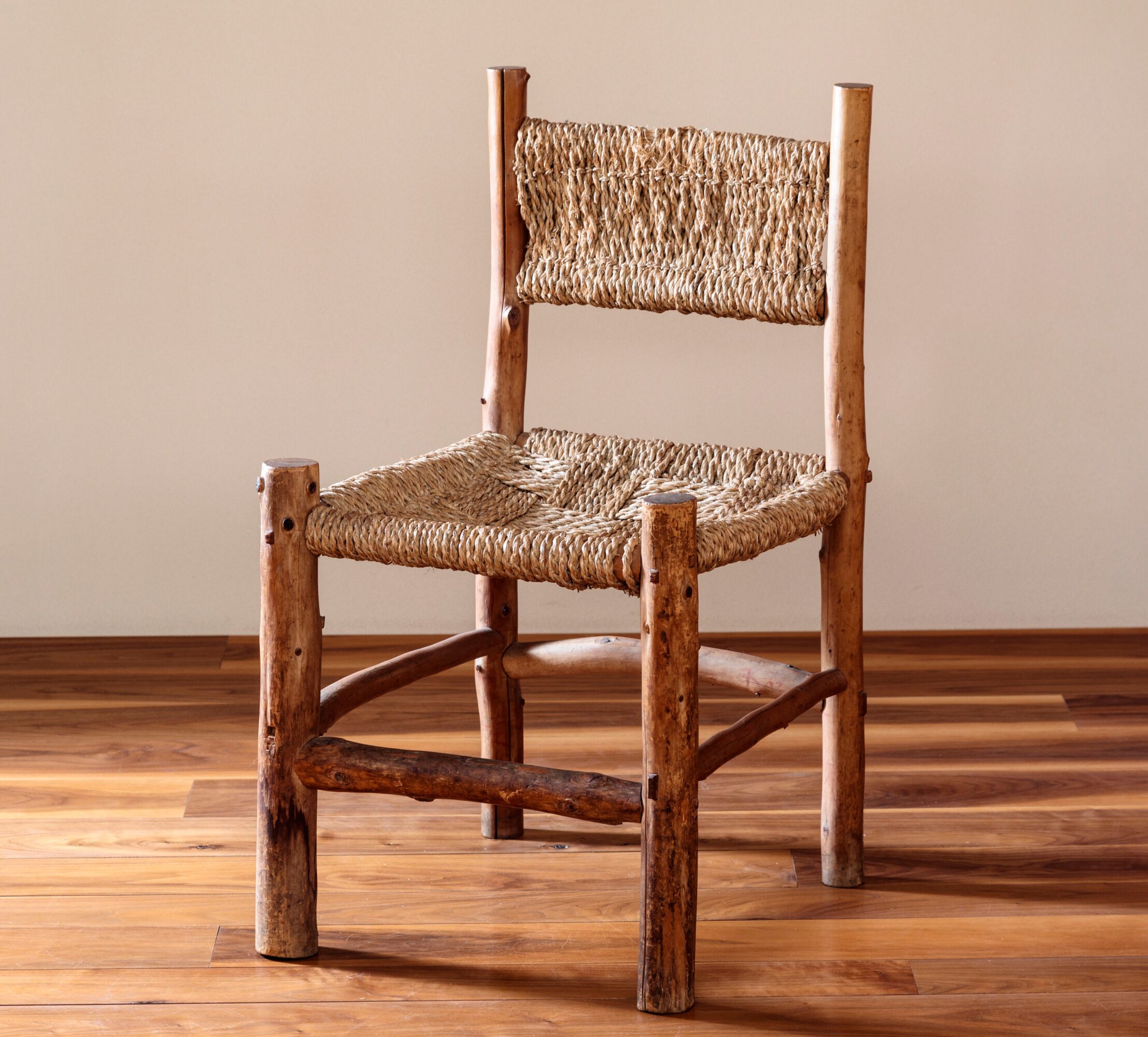 Wooden chair with woven seat and backrest, placed on a wooden floor against a plain wall.
